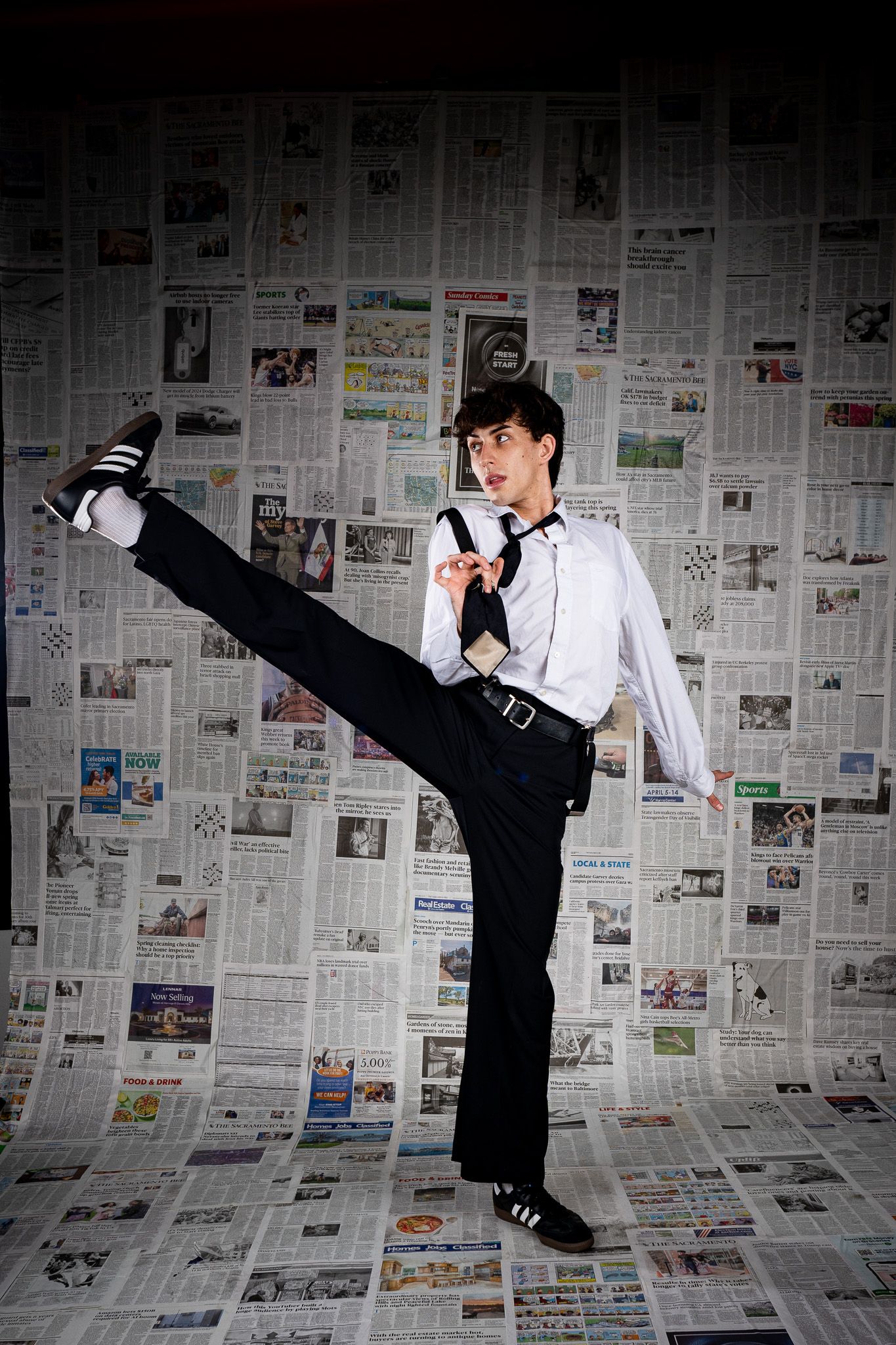 Martial artist performing high kick against newspaper backdrop wearing formal black and white attire.