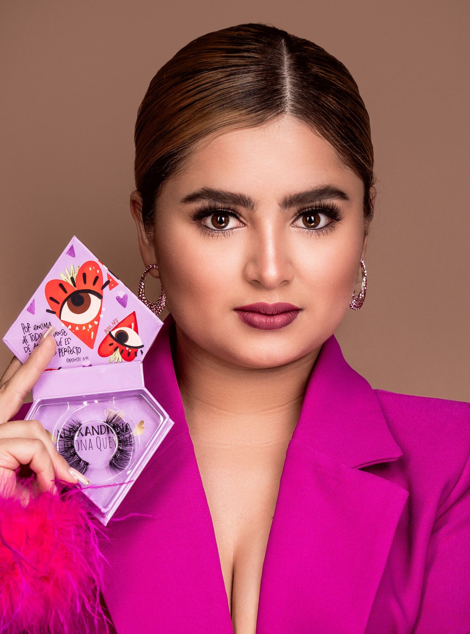 Person in magenta blazer holding makeup product packaging against brown background.