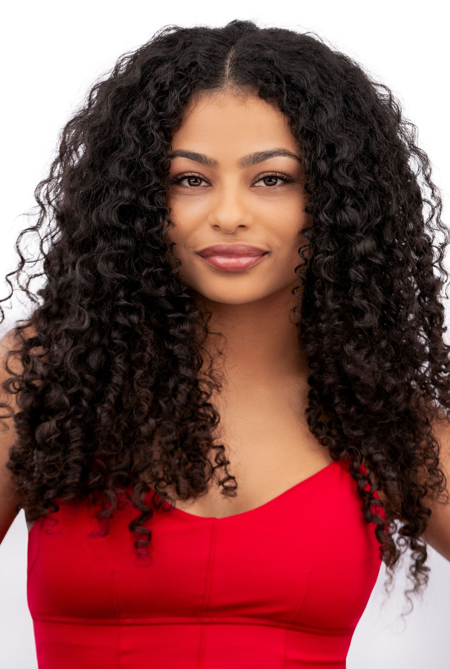 Portrait of someone with long dark curly hair wearing a red sleeveless top against a white background.