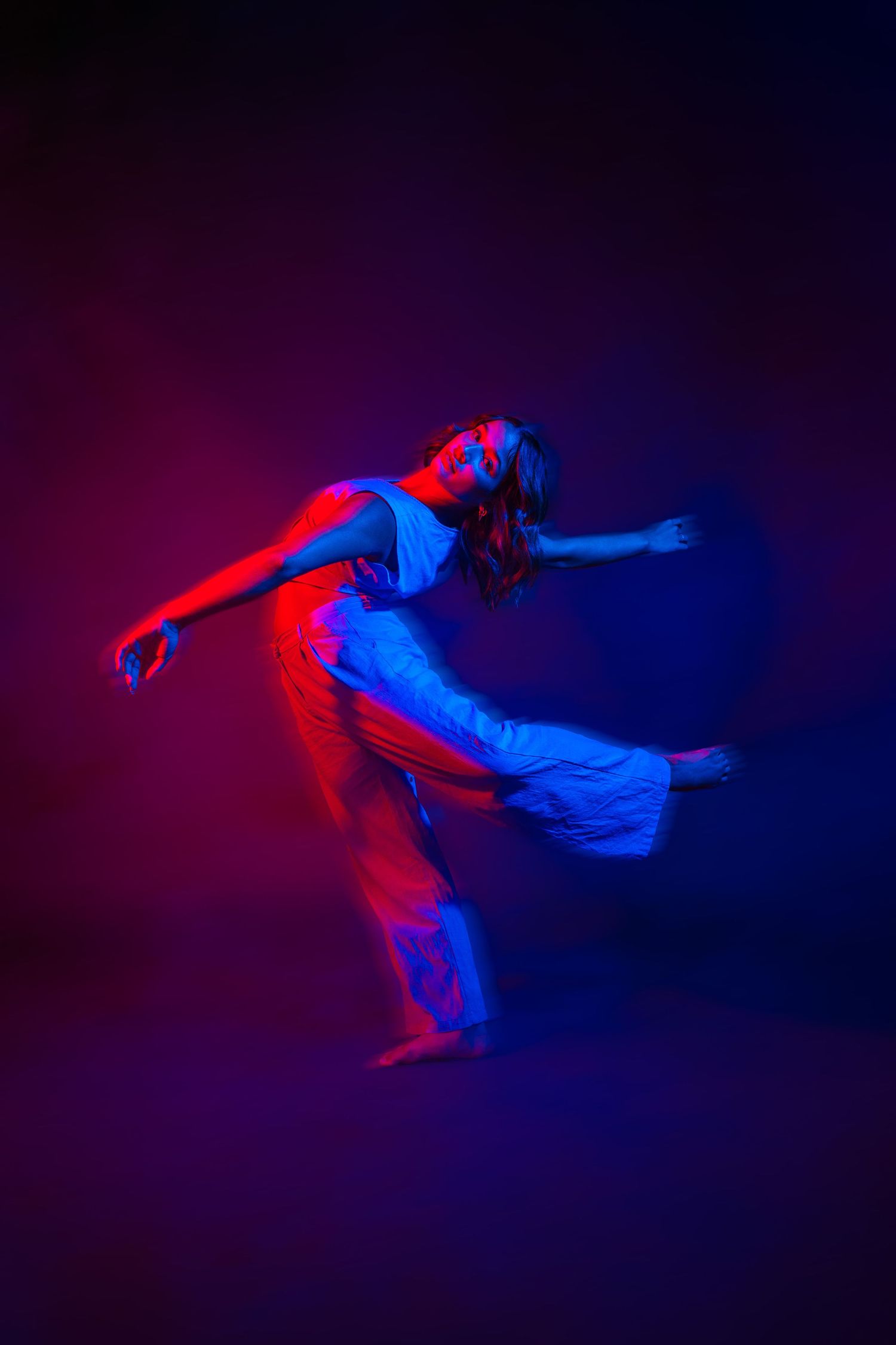 A contemporary dancer in flowing attire moves expressively under vibrant red and blue stage lighting. Vacaville Photographer