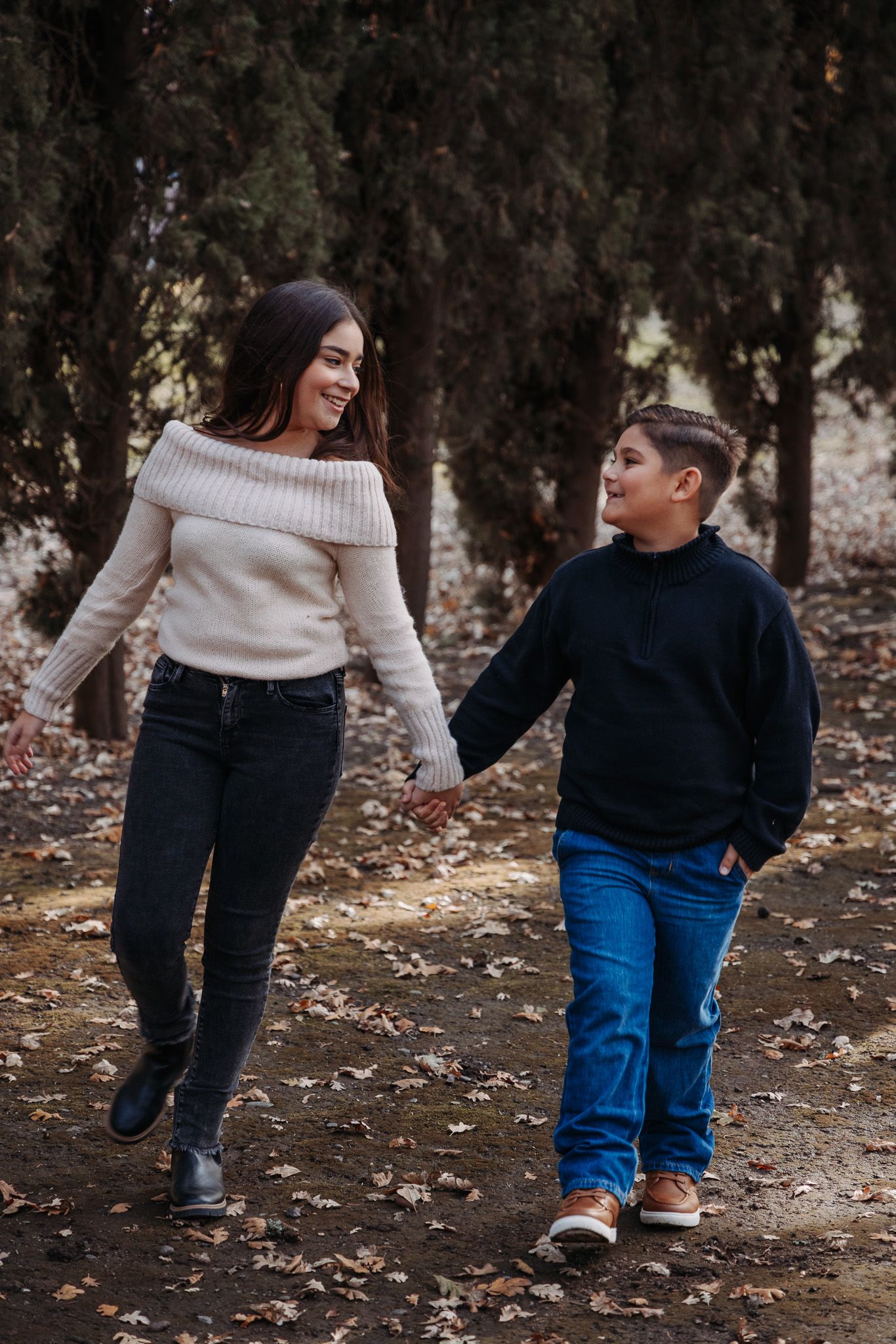 Two people walk together on fallen leaves wearing cozy sweaters and holding hands on an autumn day.