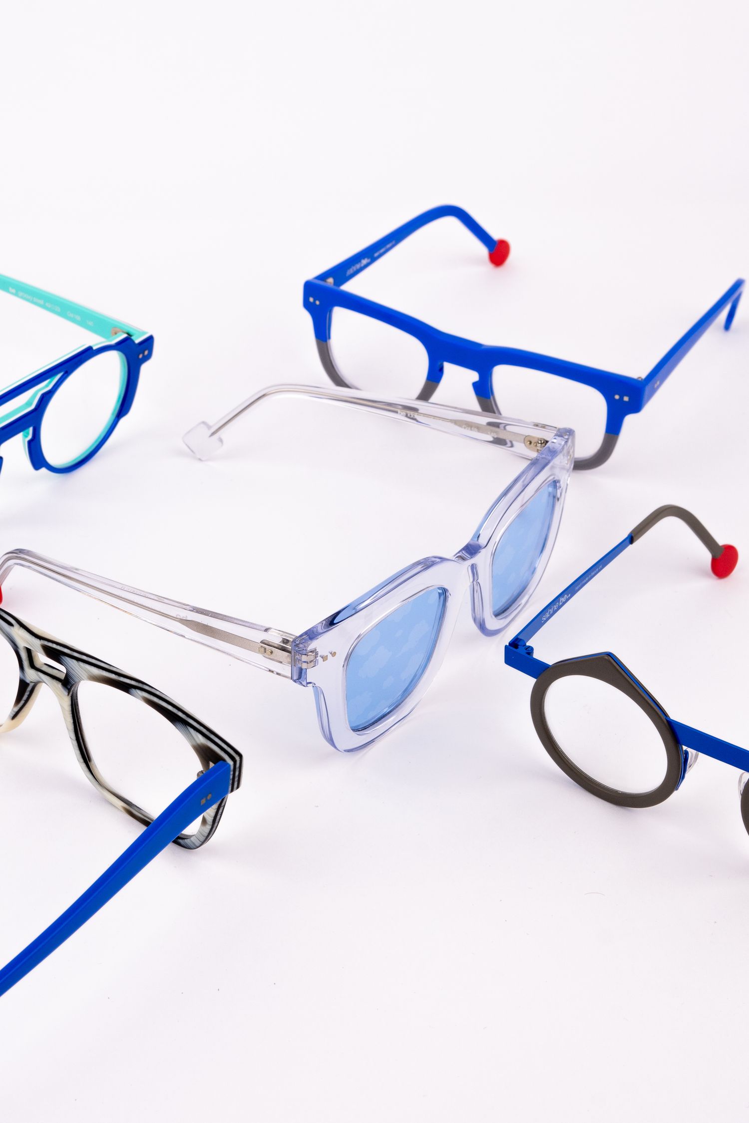 Collection of modern eyewear frames in blue, clear, and black colors arranged on white surface.