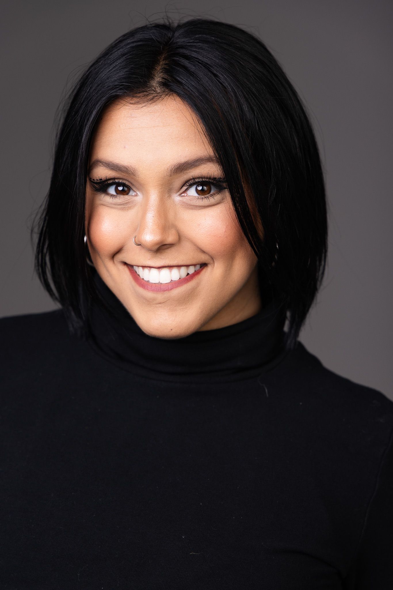 Professional headshot portrait of someone wearing a black turtleneck sweater with a bright smile against dark background.