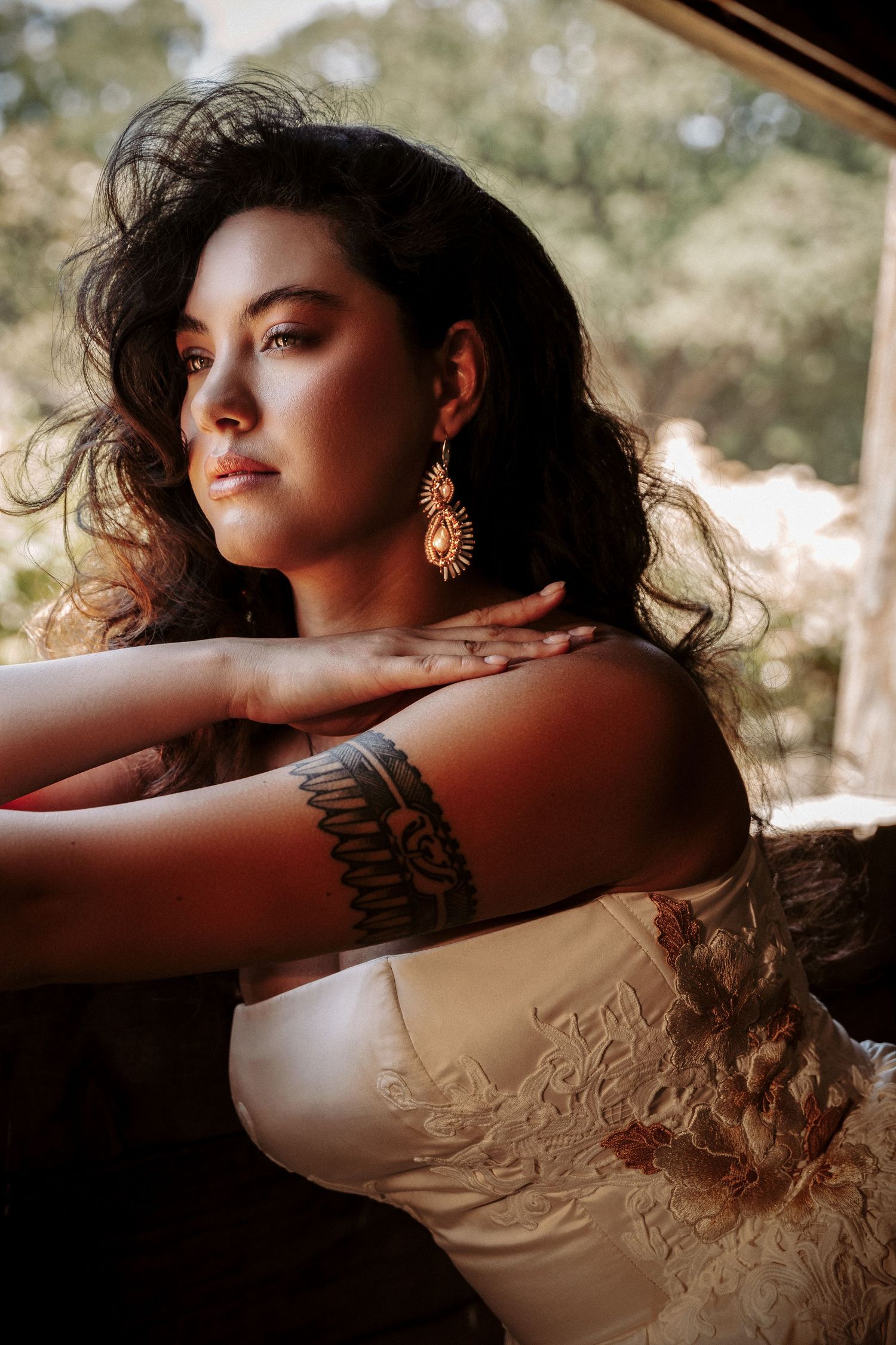 Artistic portrait with sunlit waves of dark hair and antique gold earring against soft natural lighting.