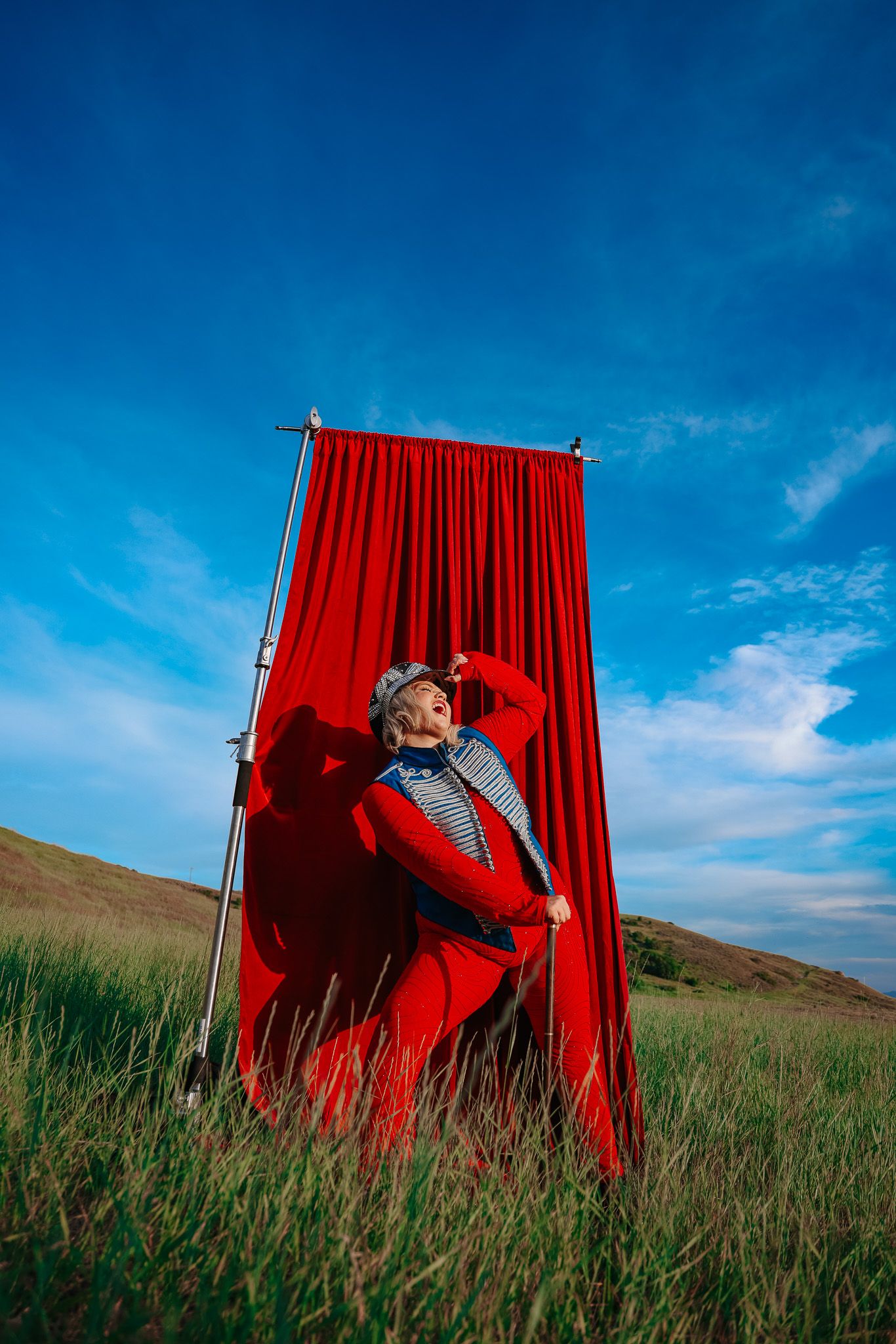 A dramatic red curtain stands in a grassy field against blue sky creating a theatrical outdoor scene.