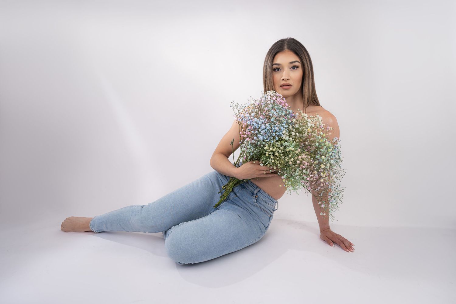 Person in light blue jeans poses on white backdrop holding delicate baby's breath flowers.