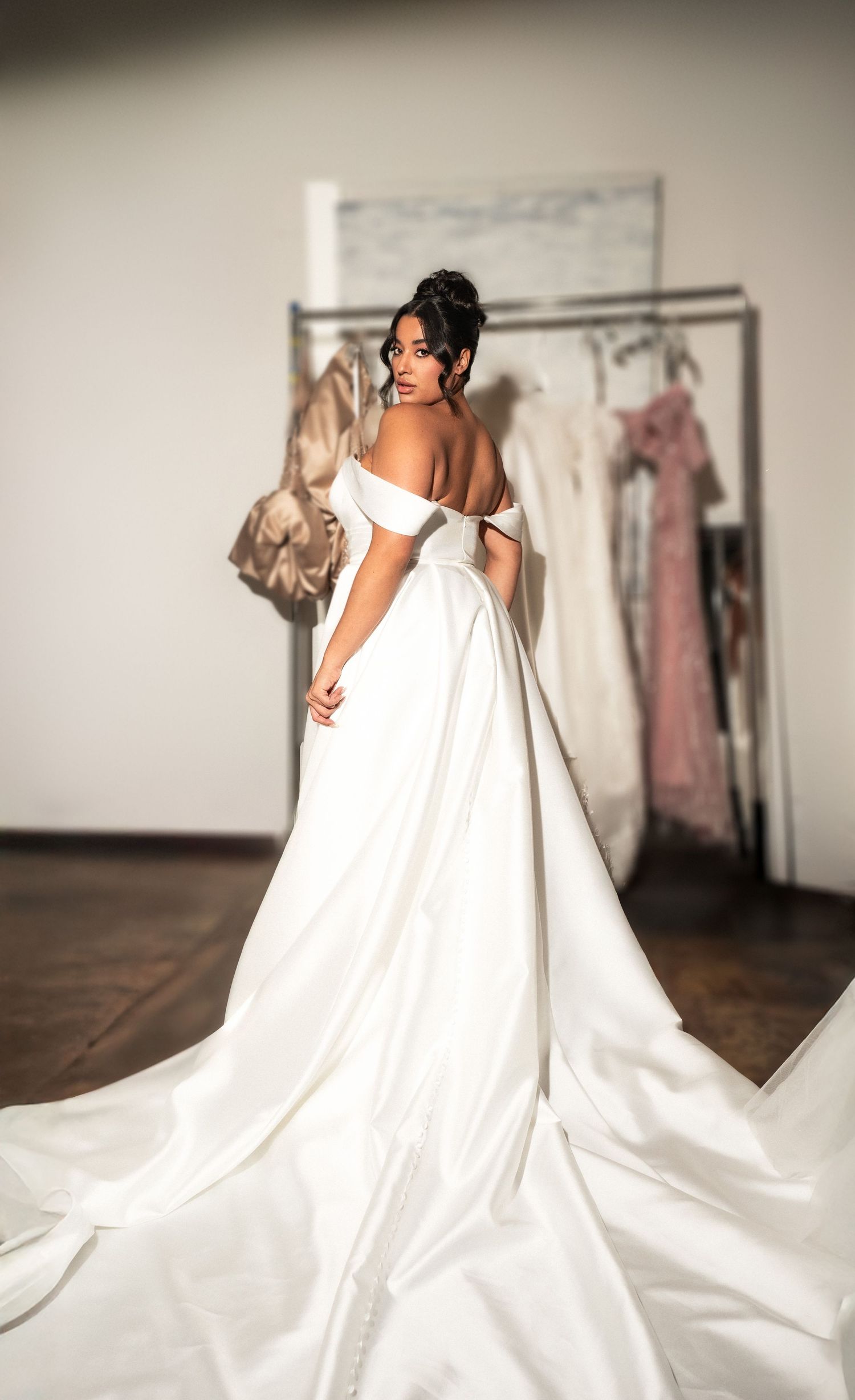 Person wearing an elegant off-shoulder white wedding gown with a flowing train in a bridal boutique setting.