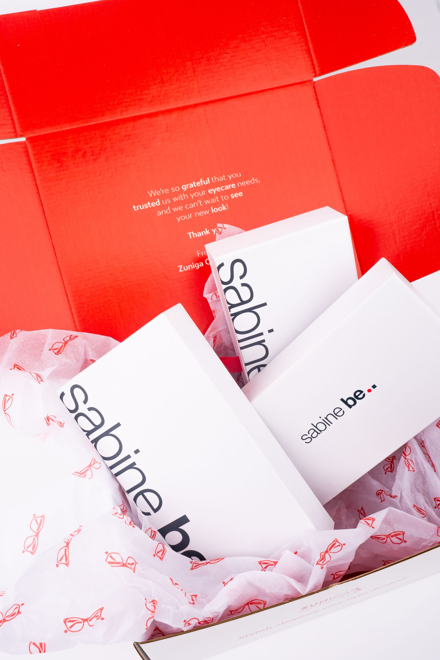 Red packaging box with Sabine Be branding materials and tissue paper.