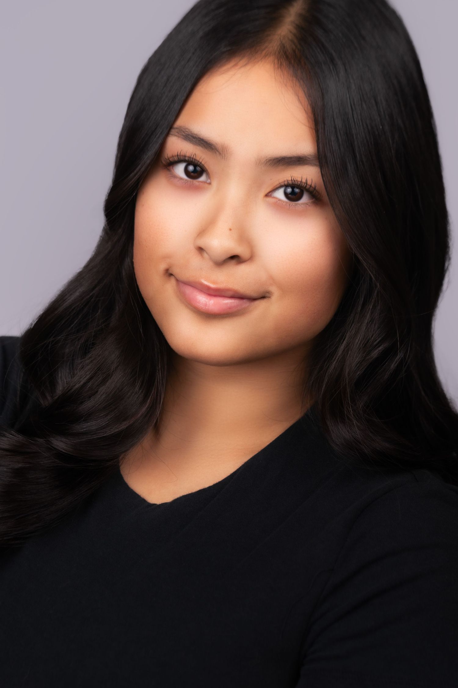 Professional headshot portrait of a person with long dark hair wearing a black top against a purple background.