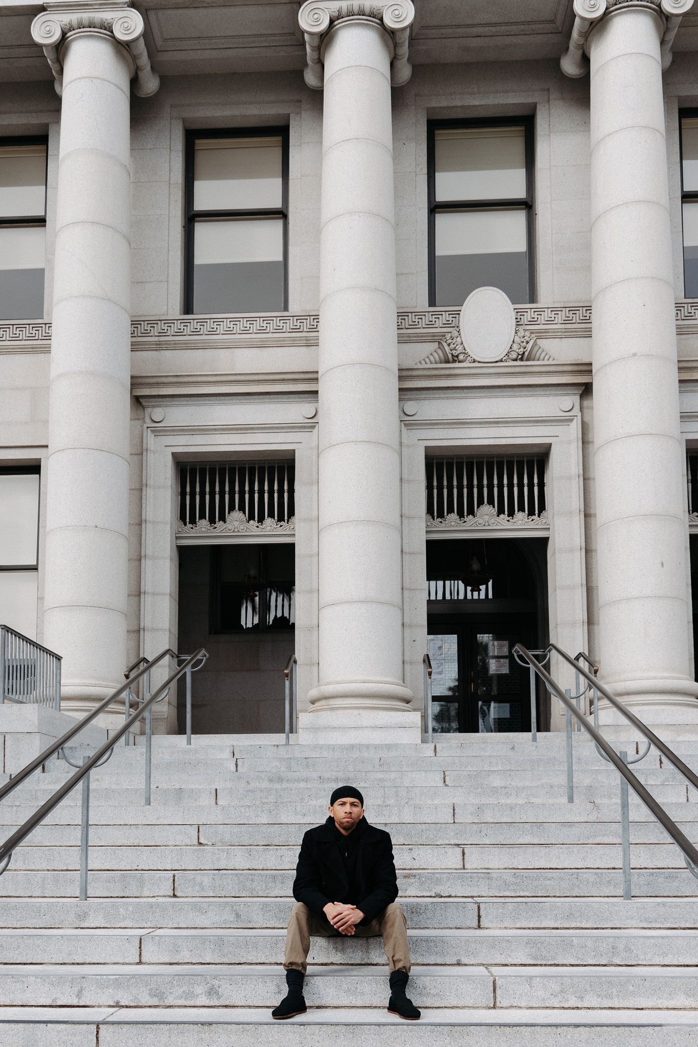 A person sits on white stone steps in front of a neoclassical building with tall ionic columns.