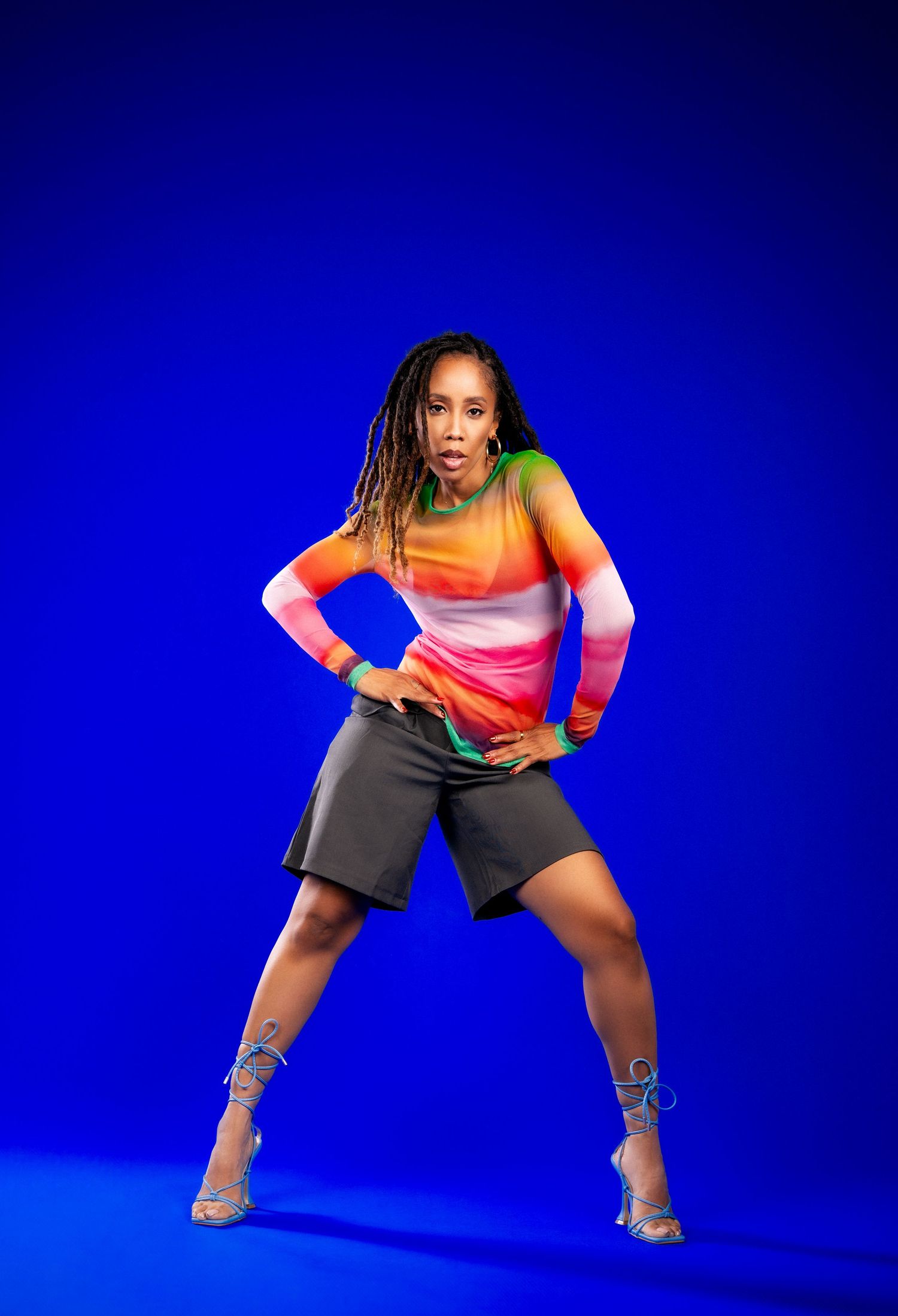 Dancer in bright ombre top and dark shorts strikes dynamic pose against vibrant blue background.