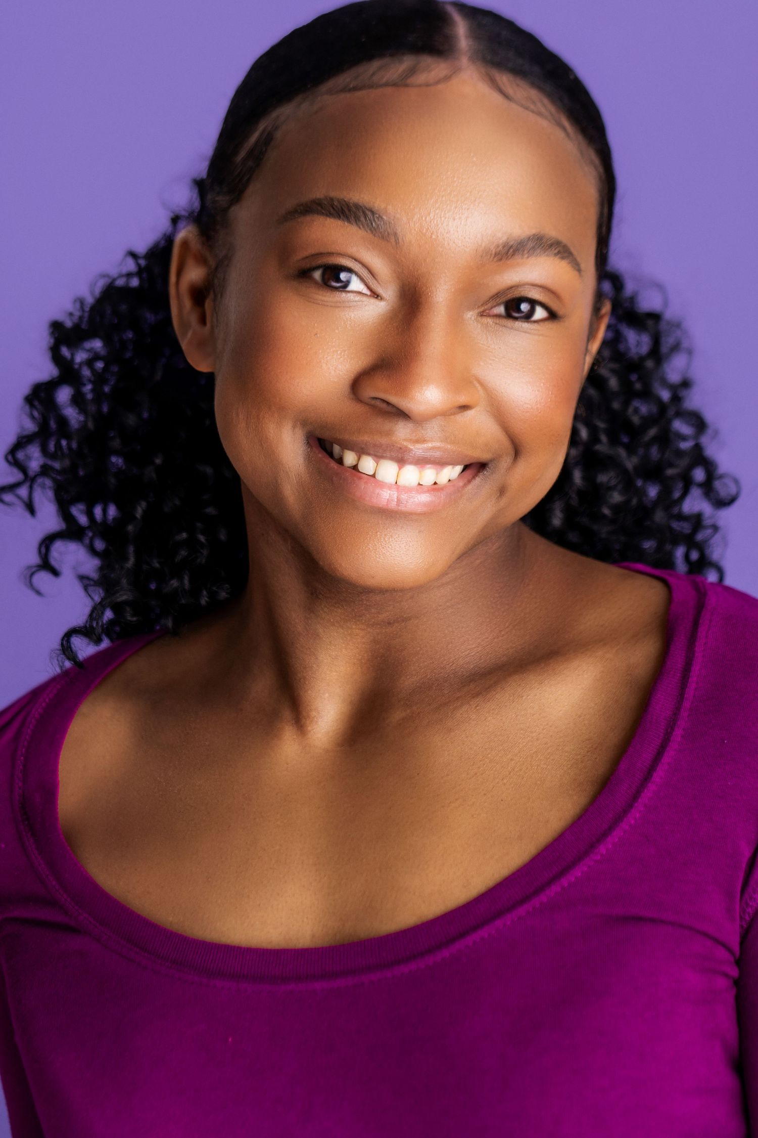Professional headshot of someone wearing a magenta top and beaming a warm, genuine smile against a purple background.