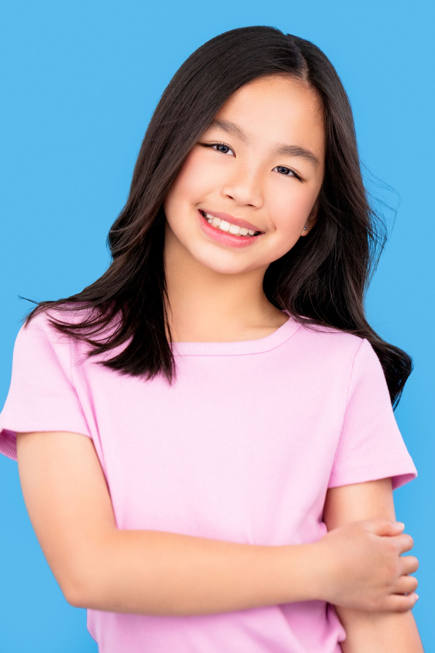 Smiling young person wearing a pink t-shirt poses against bright blue background with dark flowing hair.