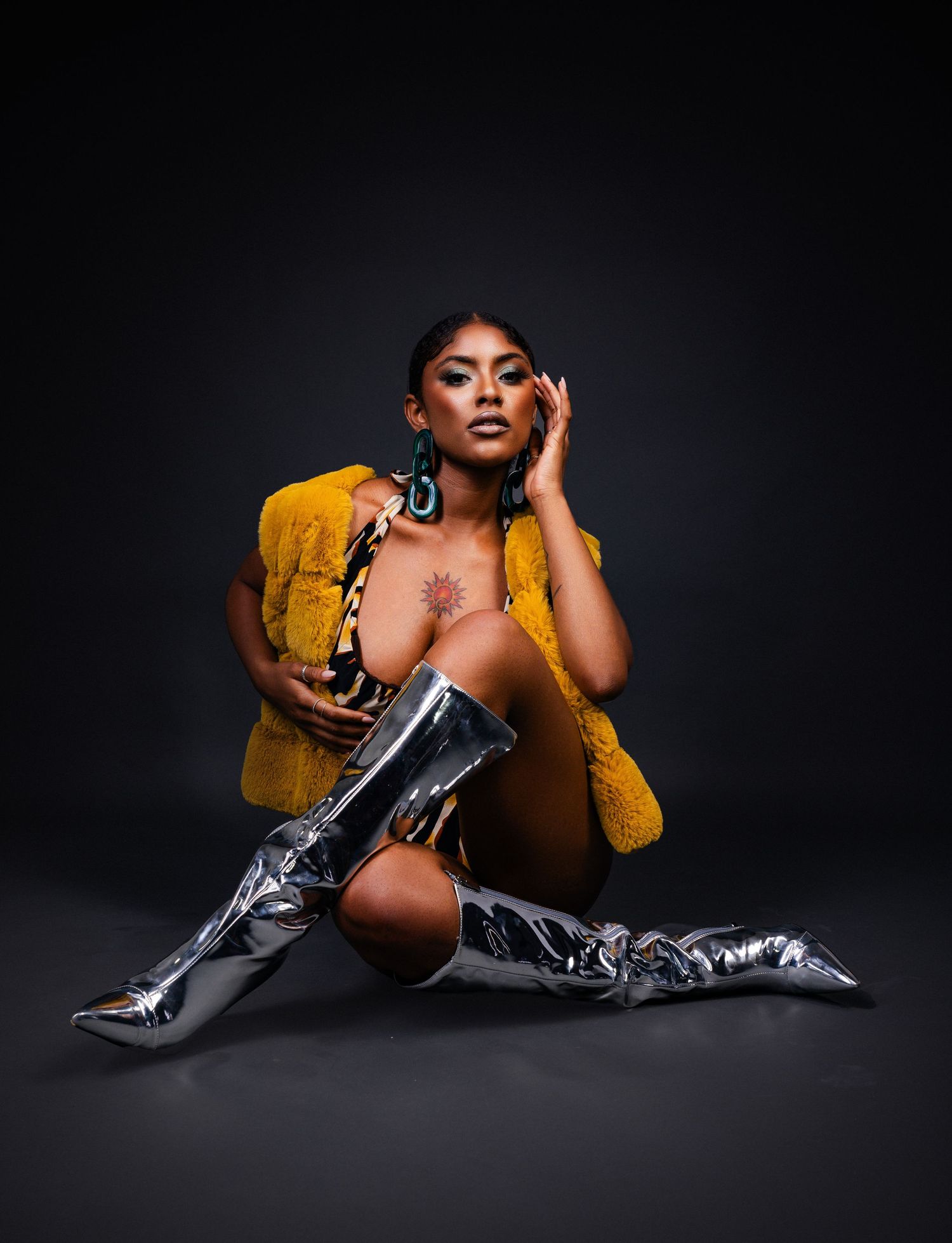 Model in yellow jacket and knee-high metallic boots poses artistically against dark background.