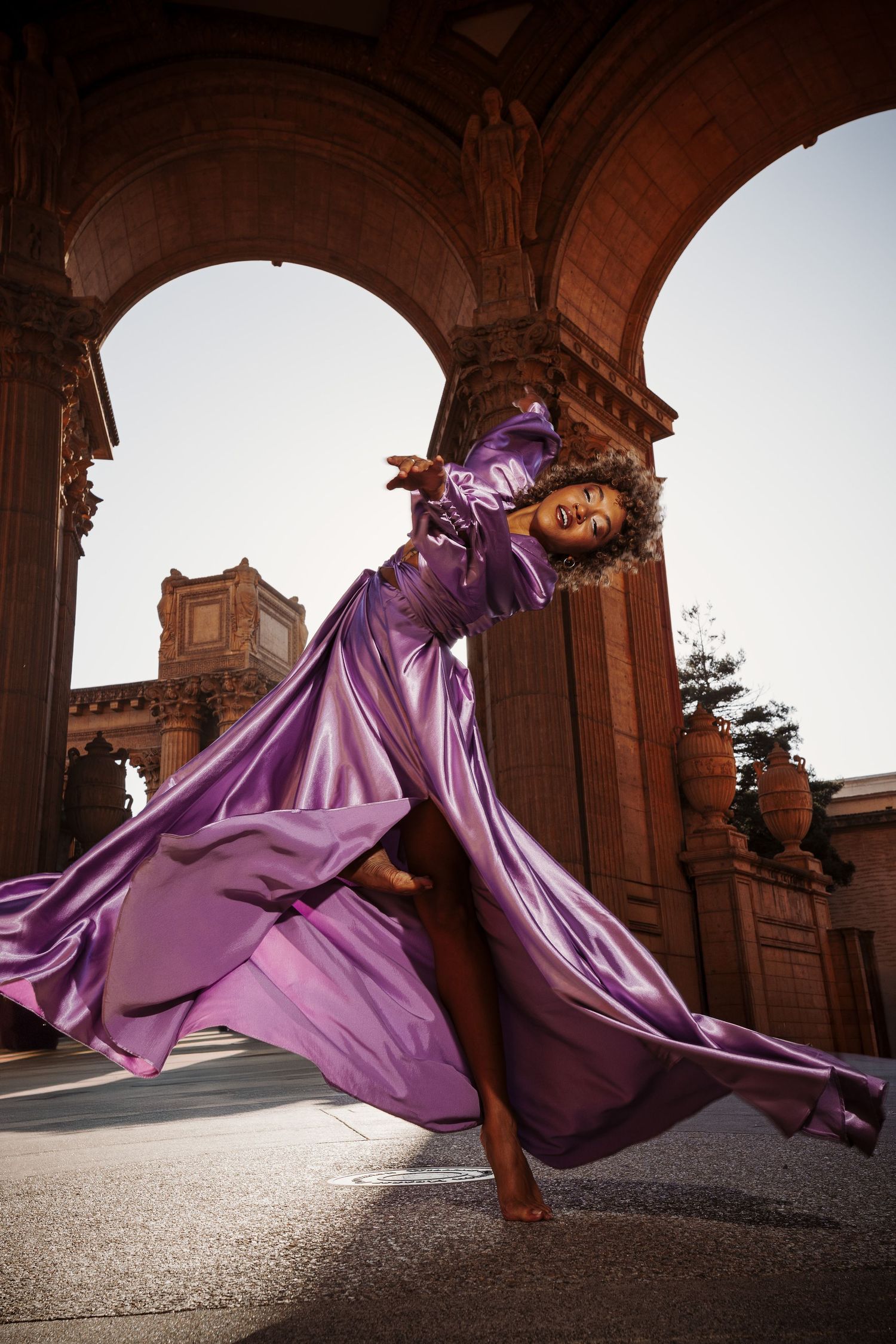 A dancer in a flowing purple gown twirls gracefully beneath ornate stone arches at the Palace of Fine Arts.