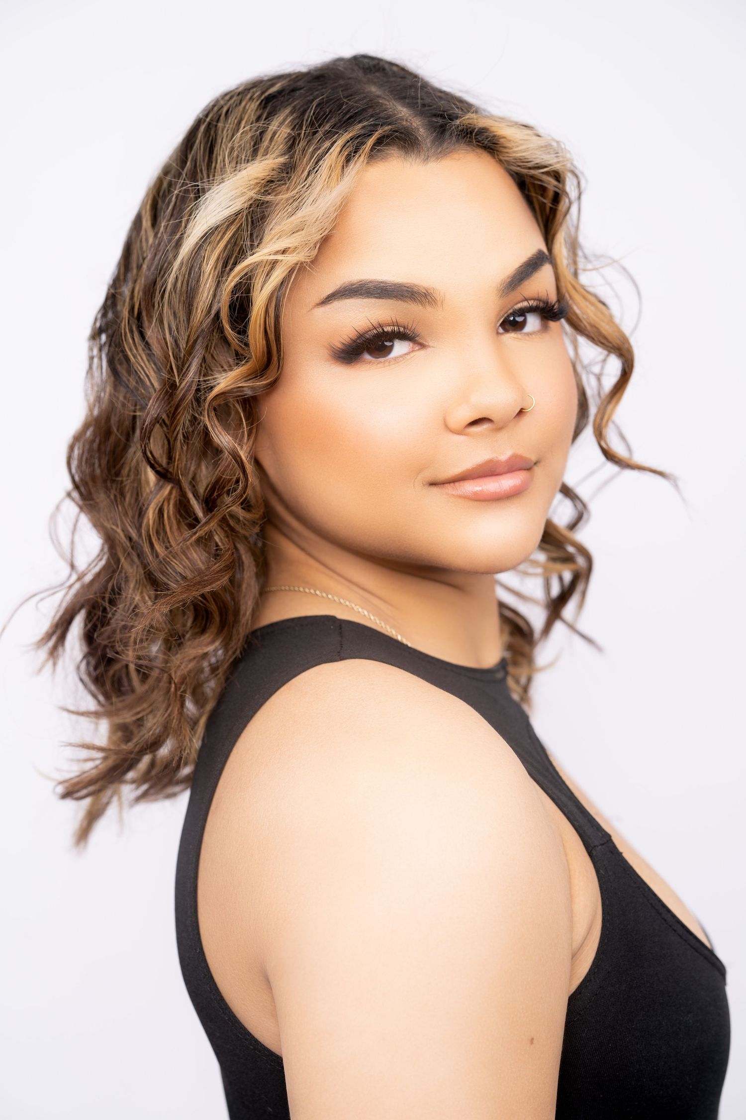Portrait of a person with wavy brunette hair wearing a black sleeveless top against a white backdrop.