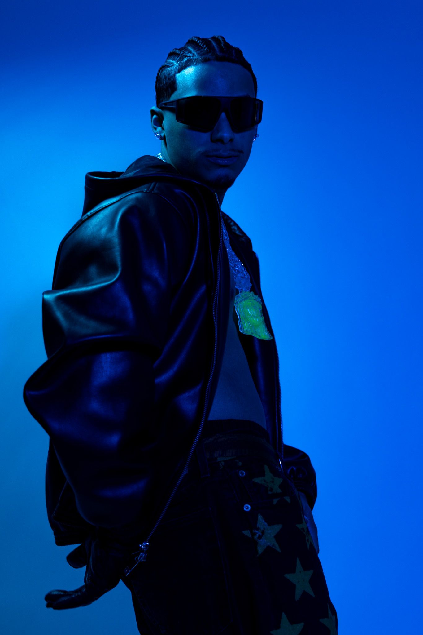 A silhouetted figure in sunglasses and a jacket poses against a deep blue backdrop with dramatic lighting.