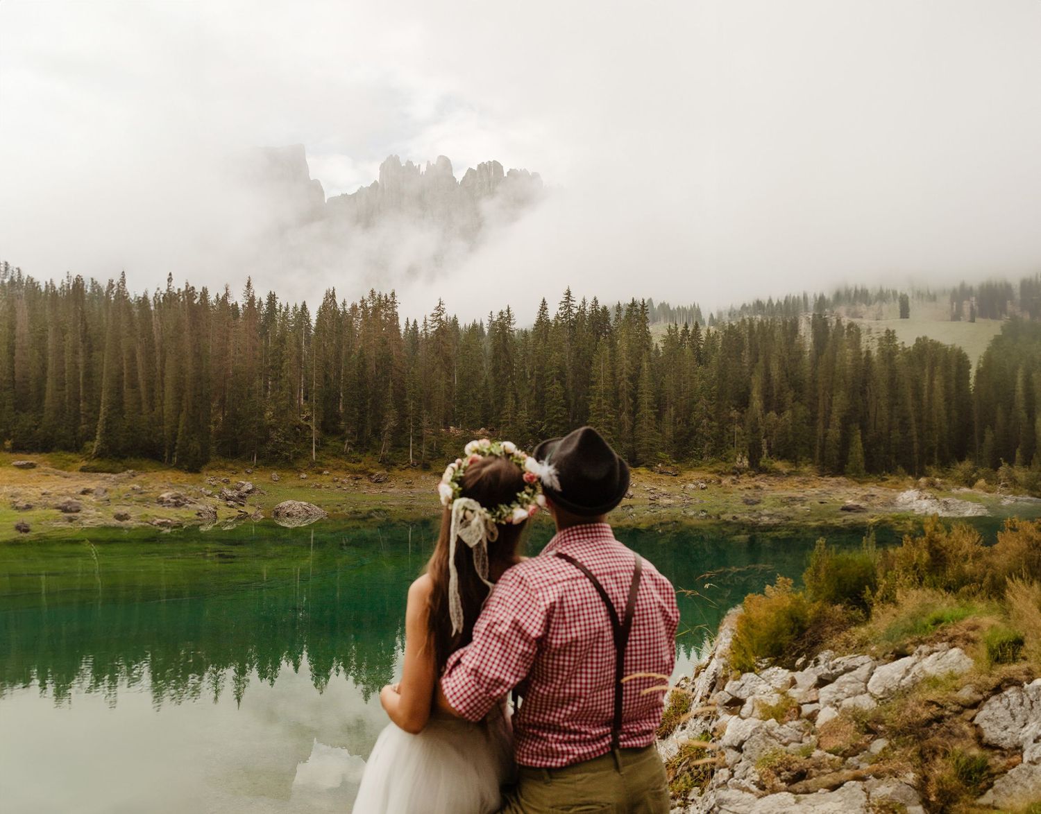 Couple admiring turquoise alpine lake surrounded by misty forest landscape.