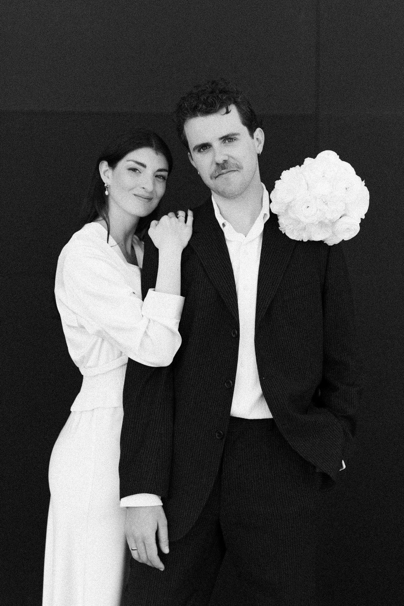 Minimalist black and white wedding photo with couple and white floral bouquet.