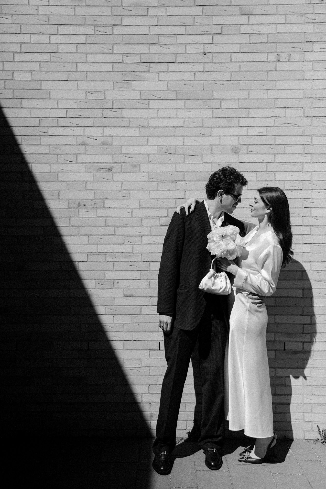 A minimalist wedding portrait against a white brick wall with strong diagonal shadows.