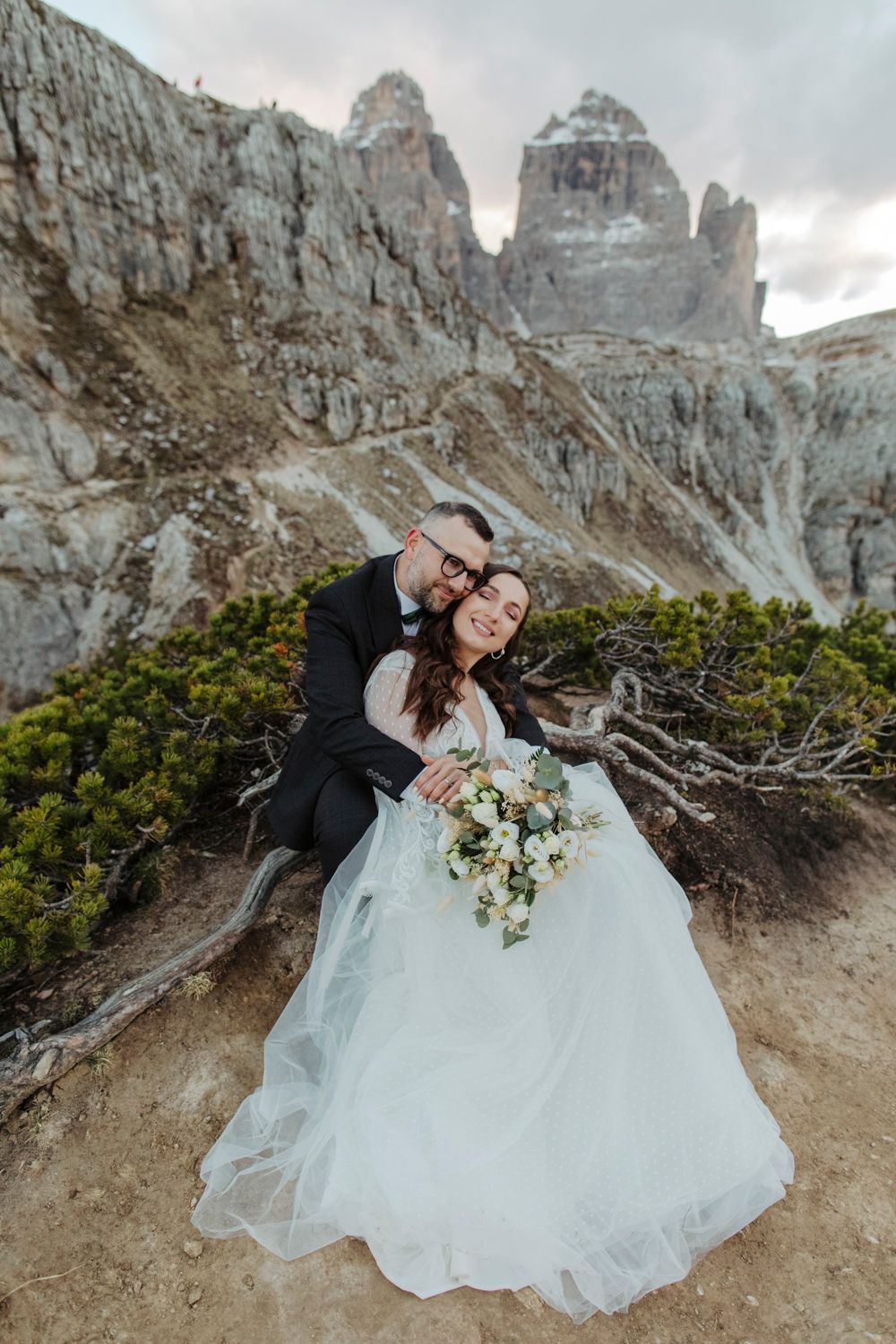Wedding portrait against rugged Dolomite mountains with dramatic cloudy sky.
