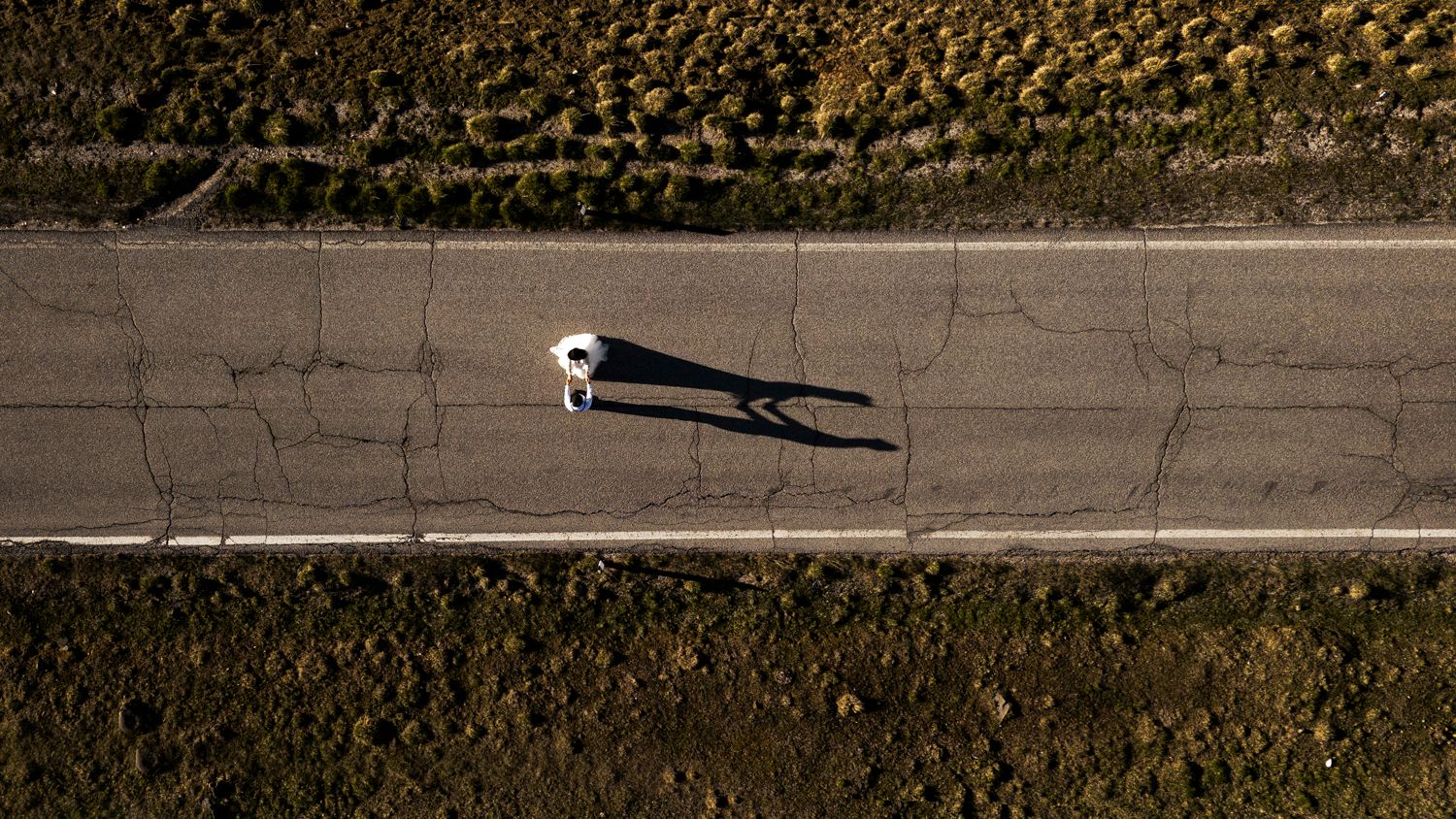 Aerial view of a car driving on a lone road through desert terrain.