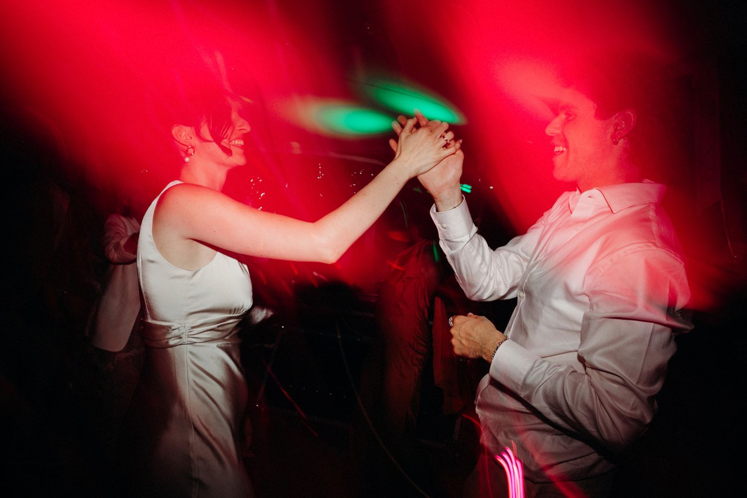Couples dancing under dramatic red lighting at an evening wedding celebration.