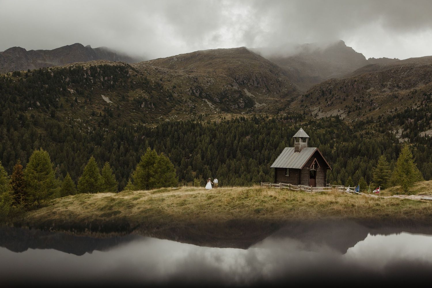 Misty mountain landscape with small chapel reflected in alpine lake.