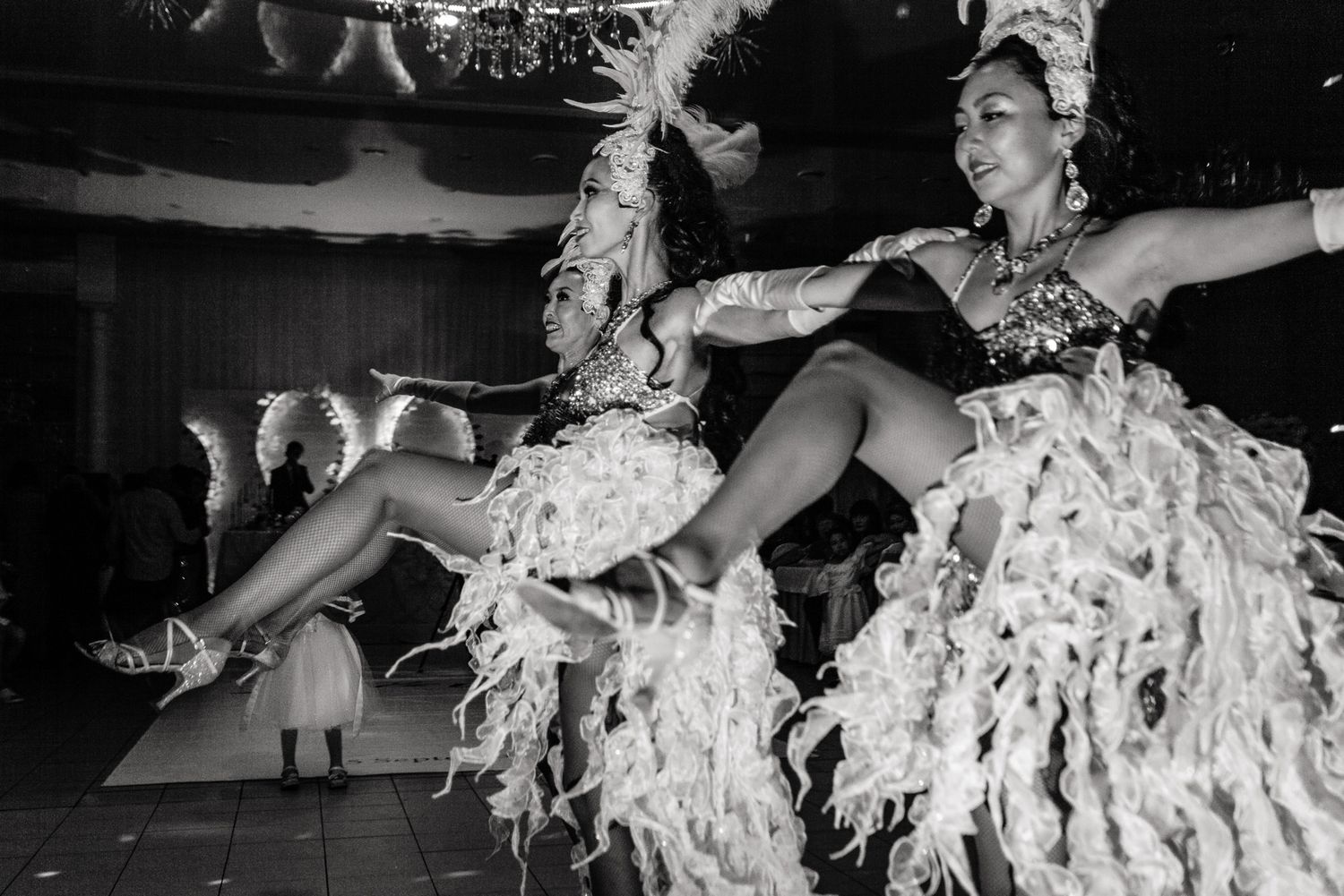 Black and white photo of dancers performing in feathered costumes during a lively cabaret show.