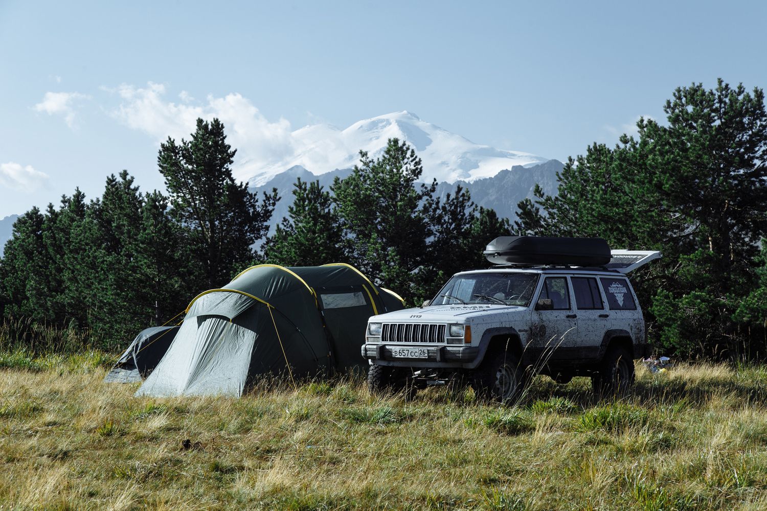 Camping scene with tents and vehicles set against mountain backdrop.