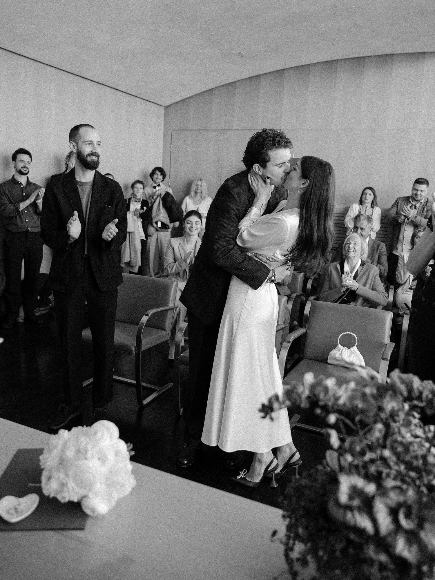Black and white reception photo showing wedding guests applauding and dancing.