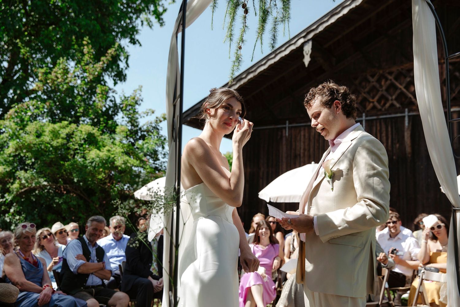 Bride and groom exchanging vows during outdoor wedding ceremony under white tent.