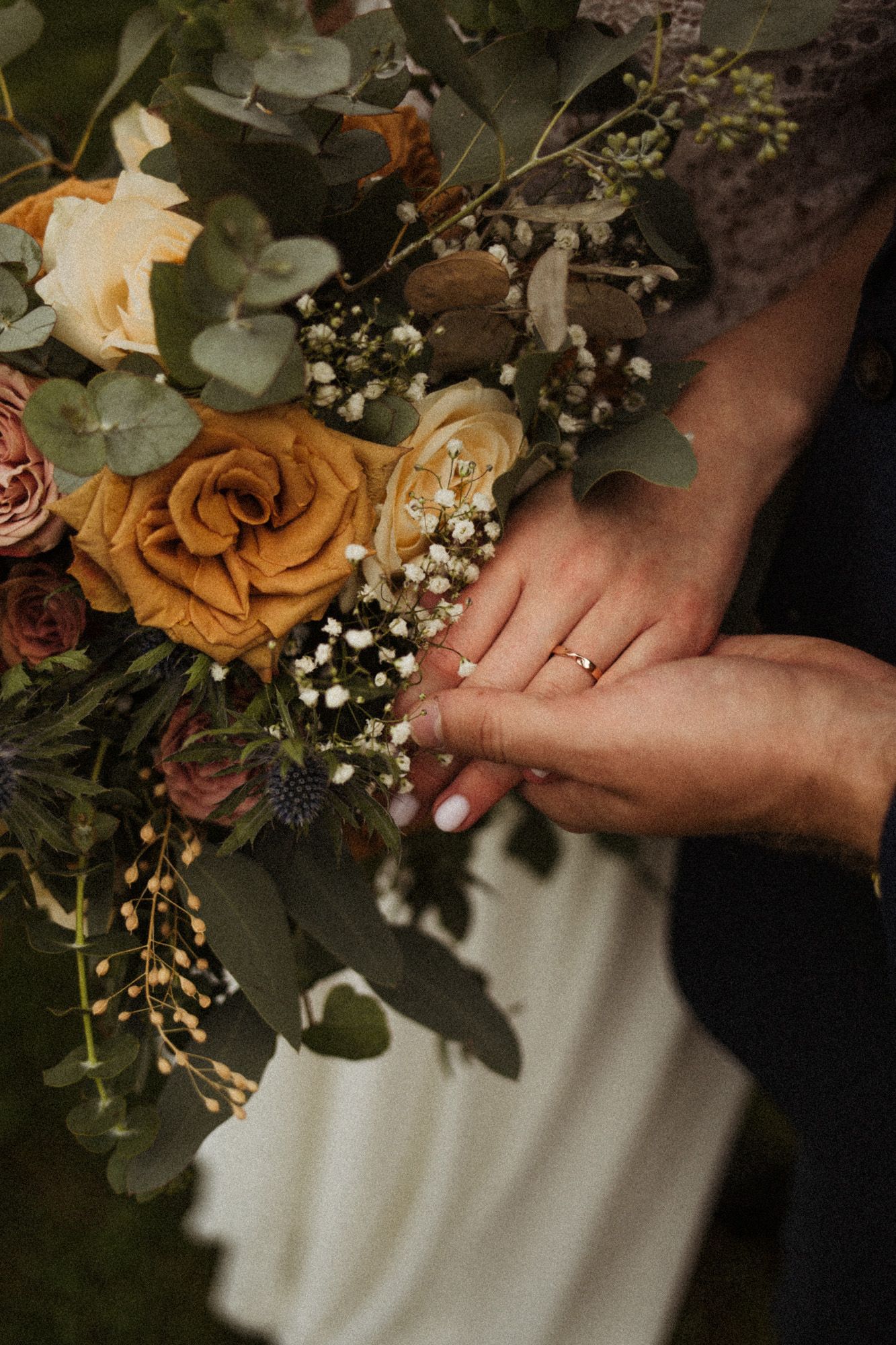 Close-up of wedding rings and a rustic bouquet featuring orange roses and baby's breath.