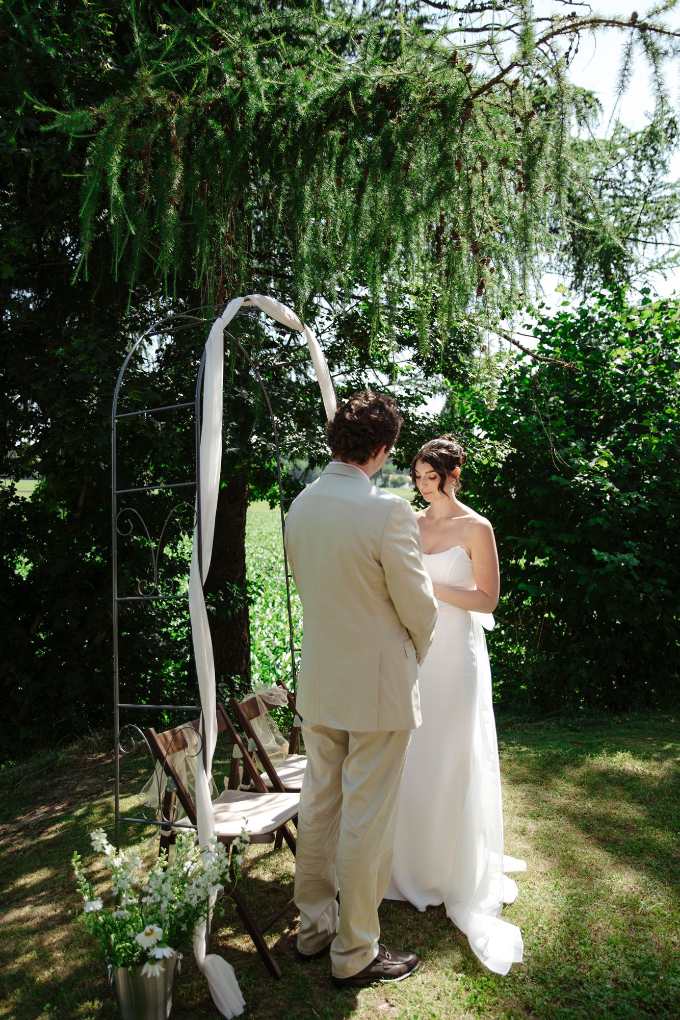 A romantic garden wedding scene with a white arch and flowing willow branches.