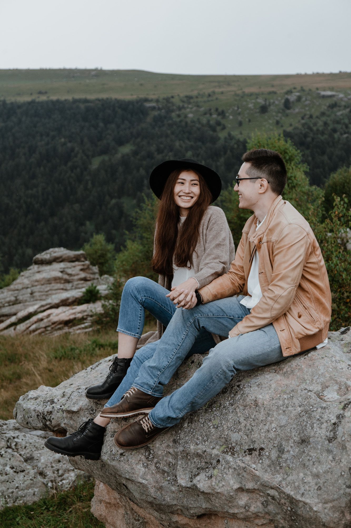 A couple relaxing on rocky outcrop overlooking a forested valley.