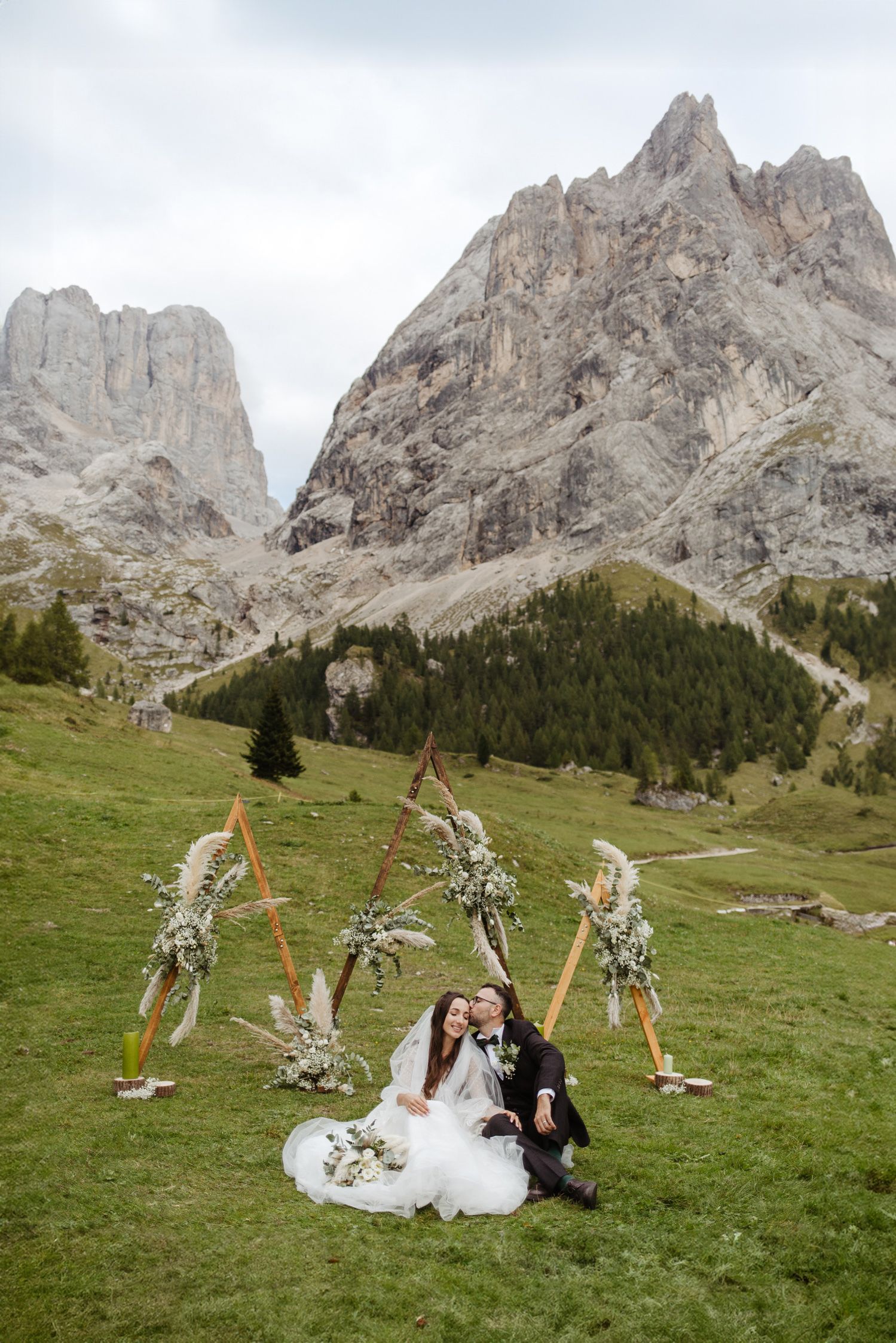 A mountain wedding ceremony setup in the Dolomites with rustic wooden arches and floral decorations against dramatic peaks.