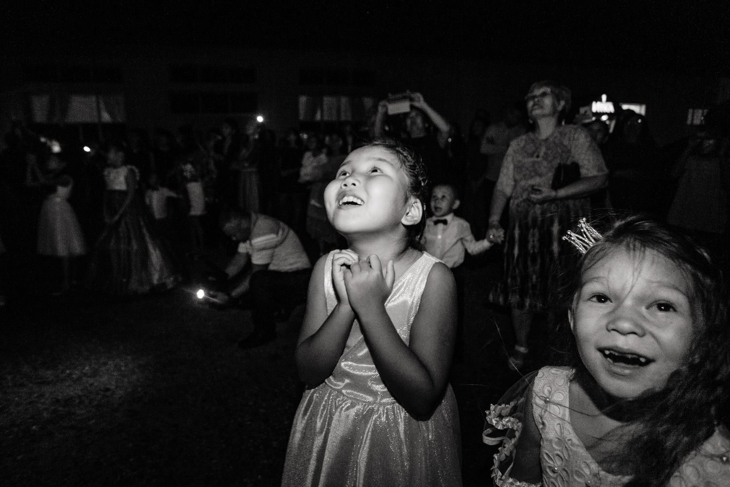 Children with excited expressions watching fireworks at an outdoor nighttime event.