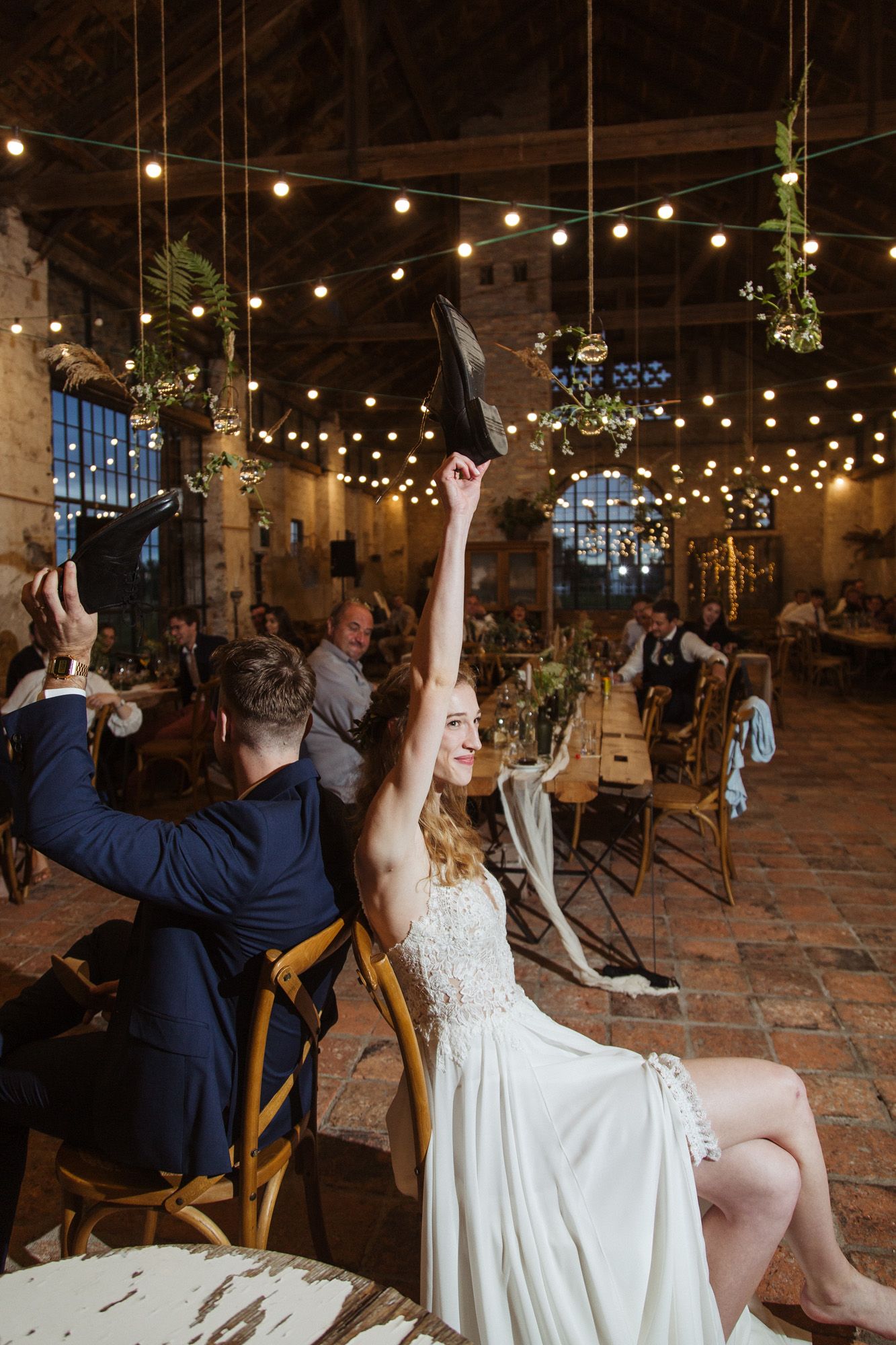 Wedding celebration moment with guests raising glasses in a string-lit brick venue.