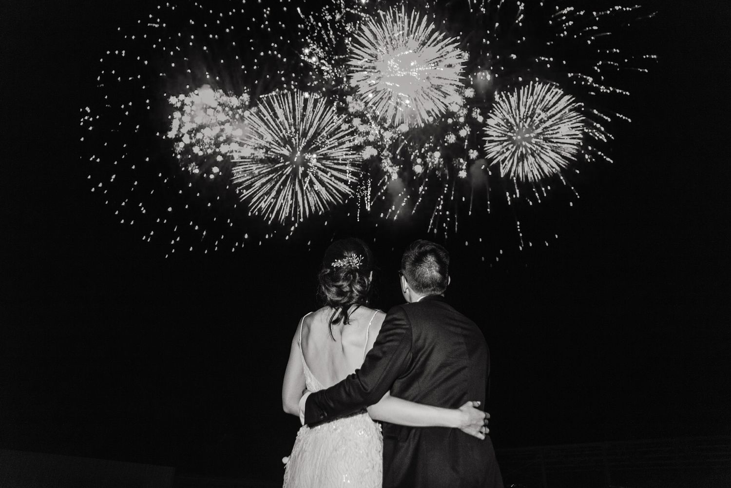 Couple embracing while watching fireworks explode in the night sky.