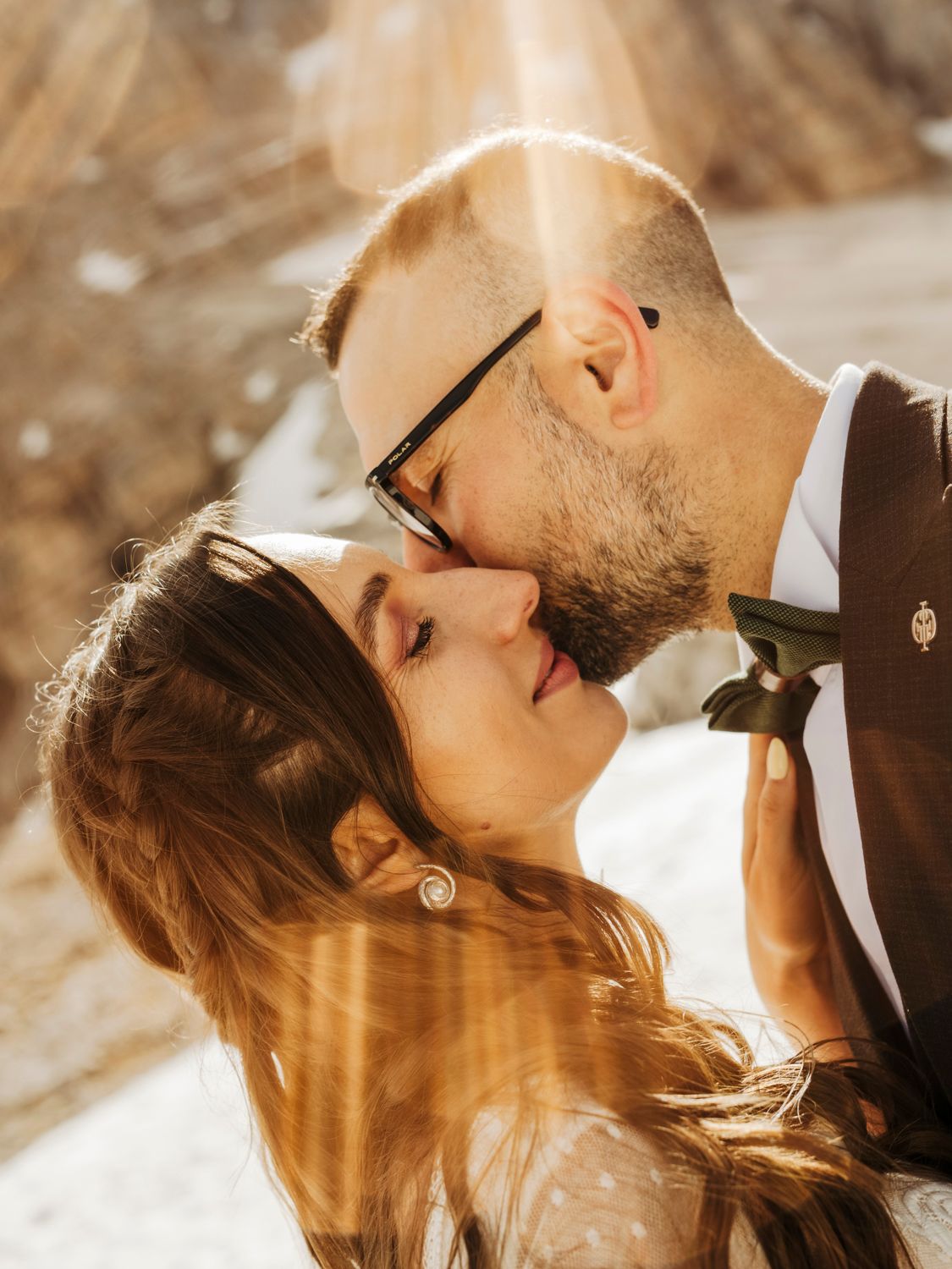 Intimate wedding moment captured in golden sunlight against mountain backdrop.