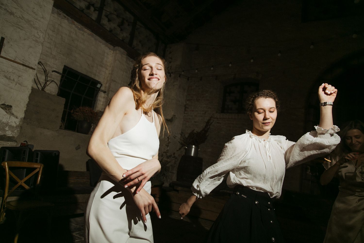 Energetic dancers move expressively in a dimly lit rustic venue.