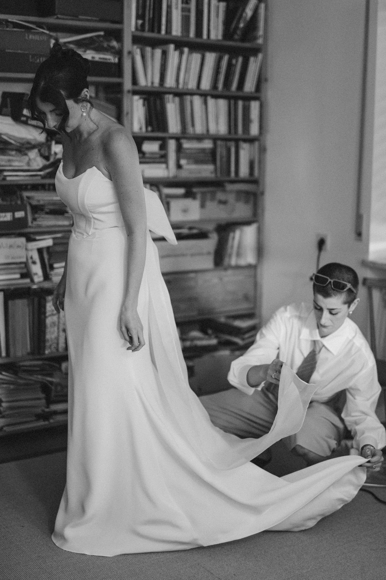Wedding dress being adjusted in library room with extensive bookshelves.