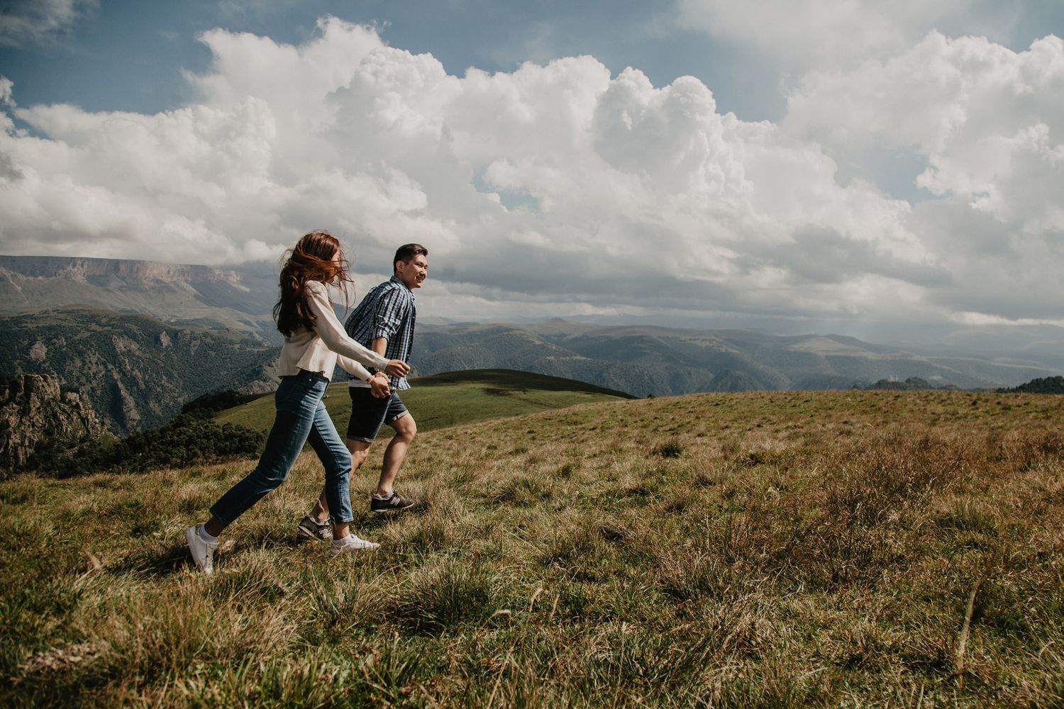 A couple hiking together through mountain terrain under cloudy skies.