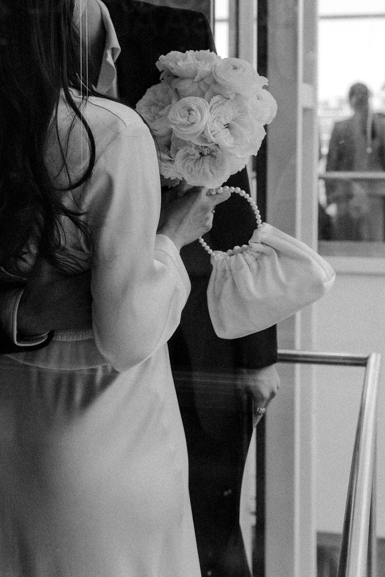 A bride in white holding a bouquet of white roses, photographed from behind in black and white.