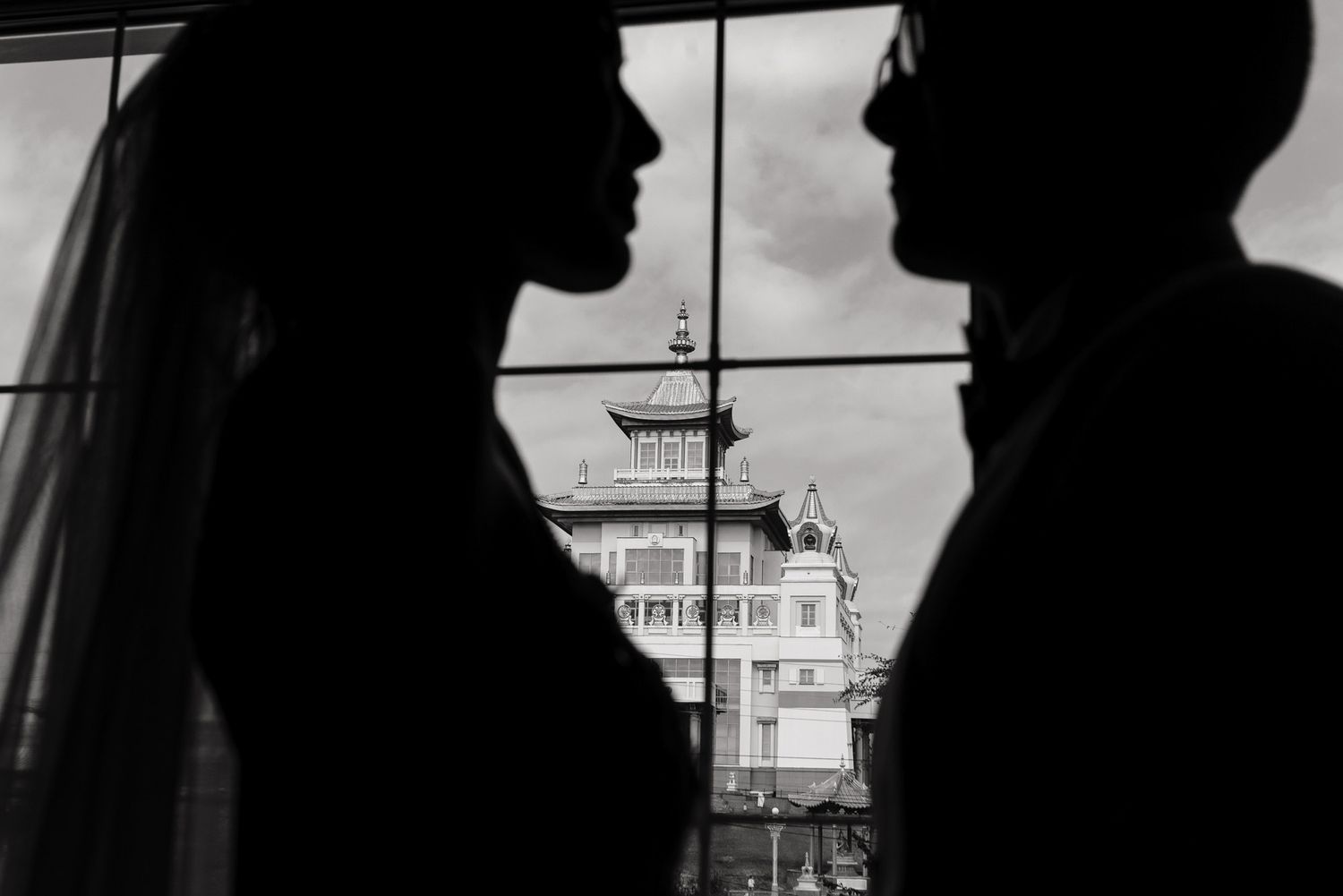 Silhouettes of a couple stand by window with Asian architecture visible in background.