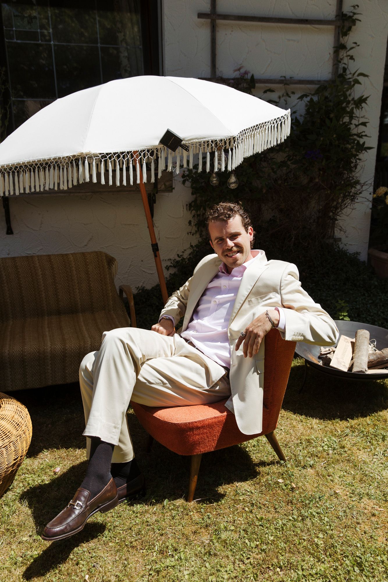 Person lounging in cream suit on orange chair in sunny garden setting.