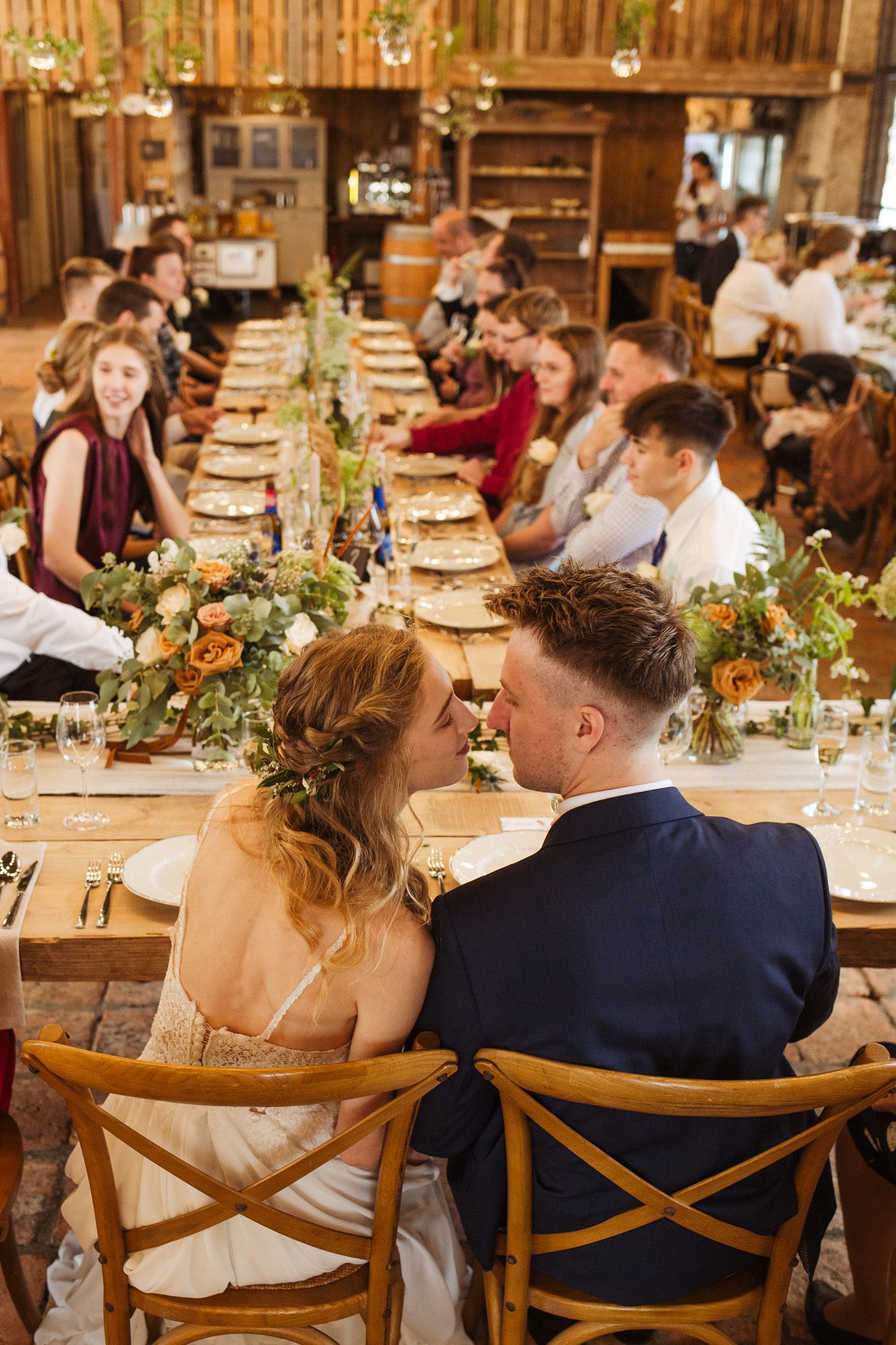 Wedding reception in rustic barn venue with long tables and floral centerpieces.