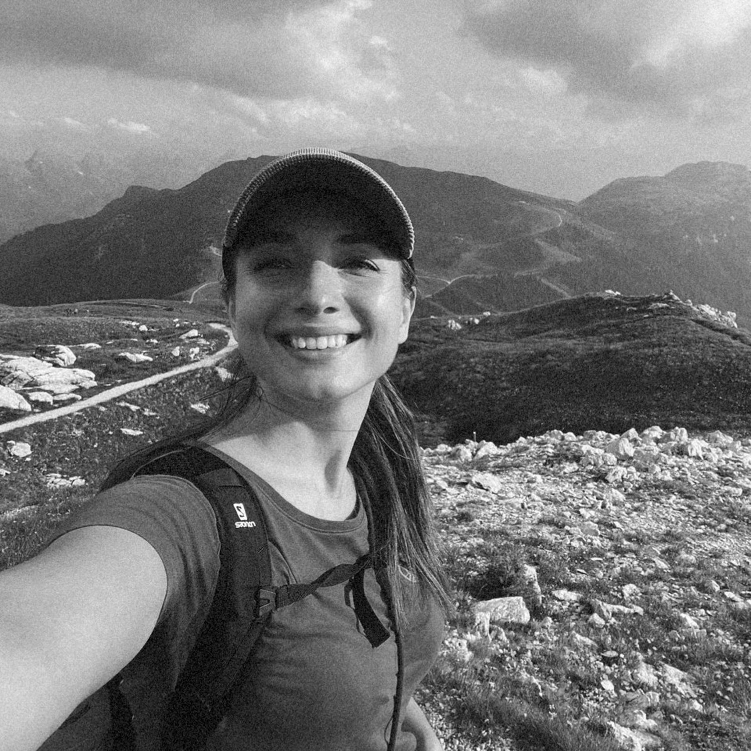 Adventurer takes selfie on rocky mountain summit with scenic valley behind.