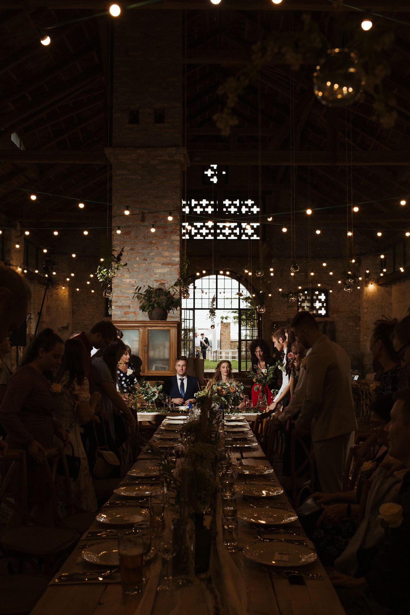Rustic wedding reception venue with string lights and exposed brick illuminated for evening dining.