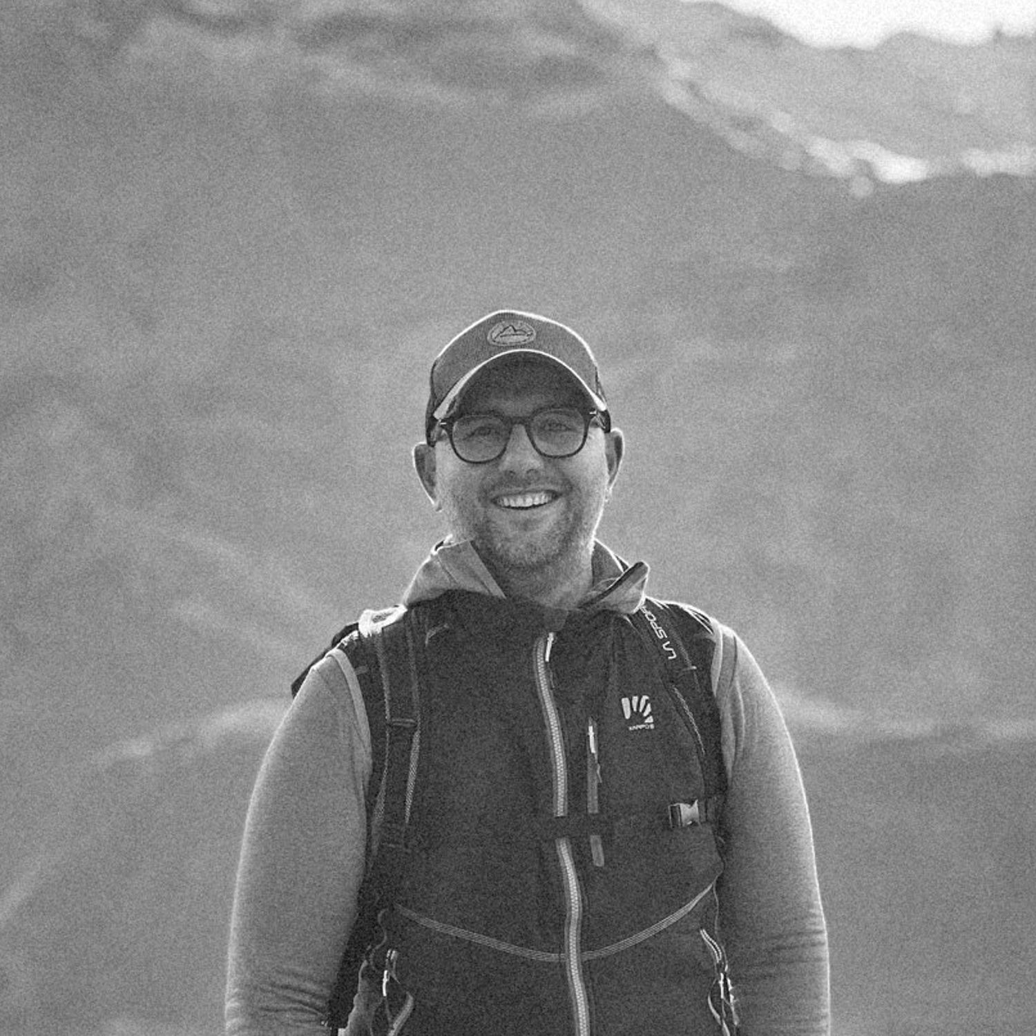 Portrait of outdoor enthusiast wearing cap and vest against mountain backdrop.